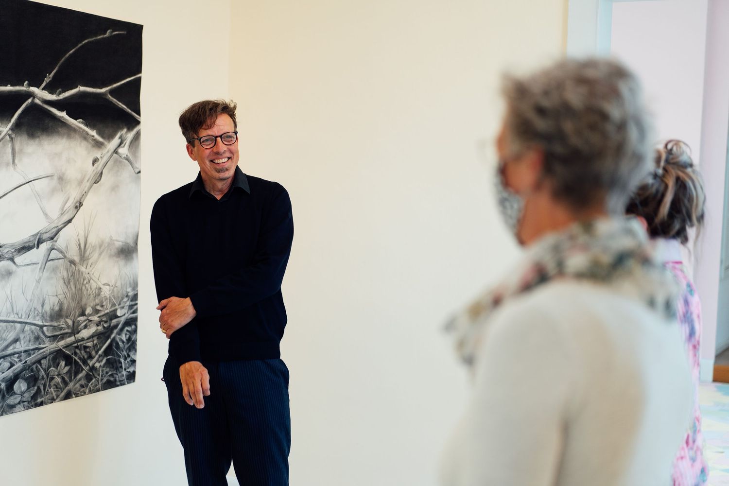 Man in black sweater smiling while discussing artwork in a contemporary art gallery.
