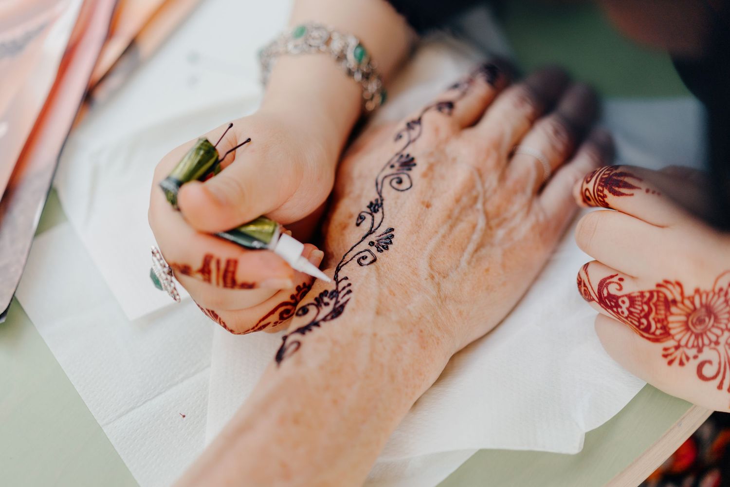 Close-up of artist applying intricate henna tattoo design on a person's hand.