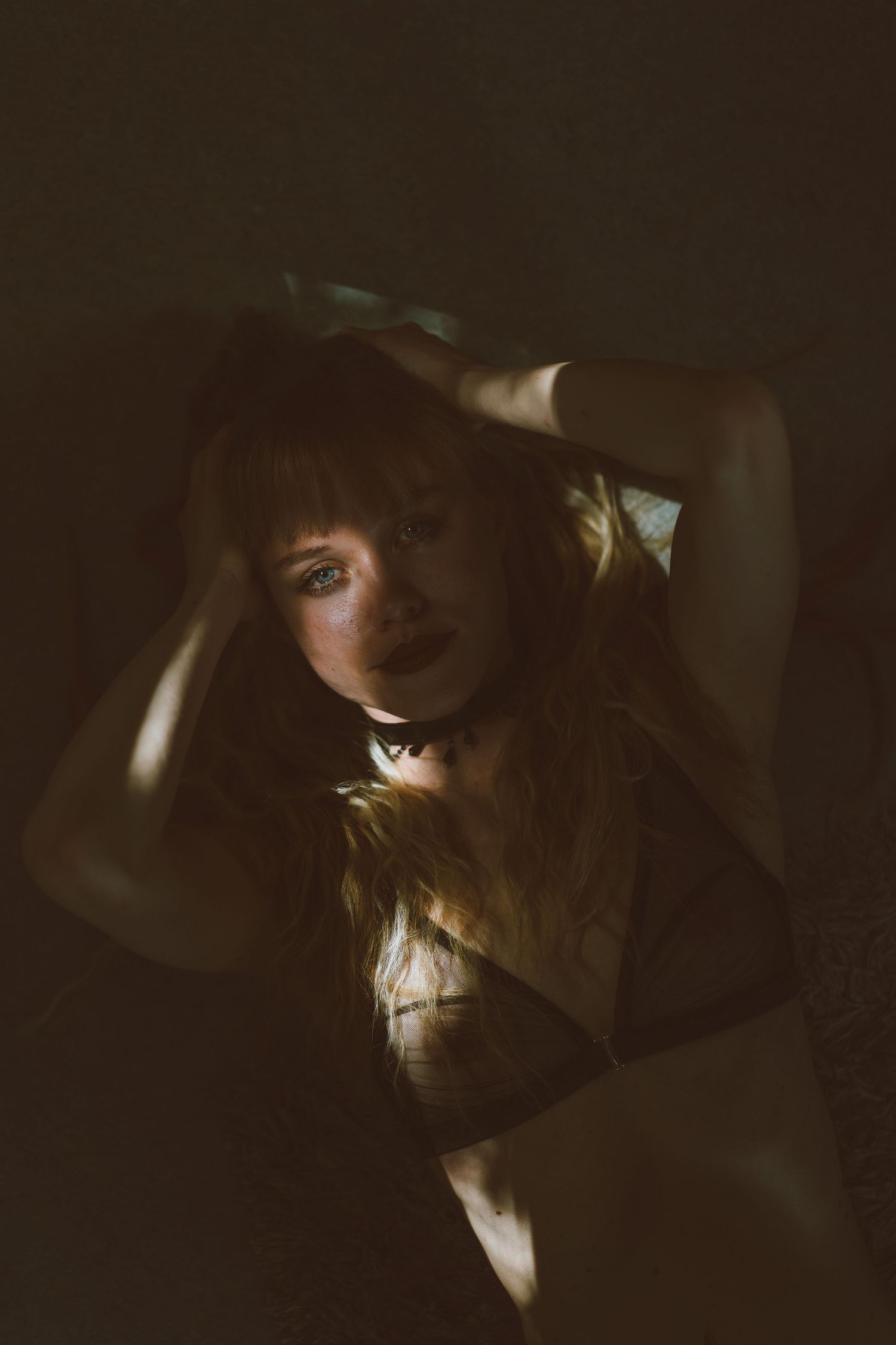Moody portrait of redhead woman with hands in hair, dramatic shadow light across face.