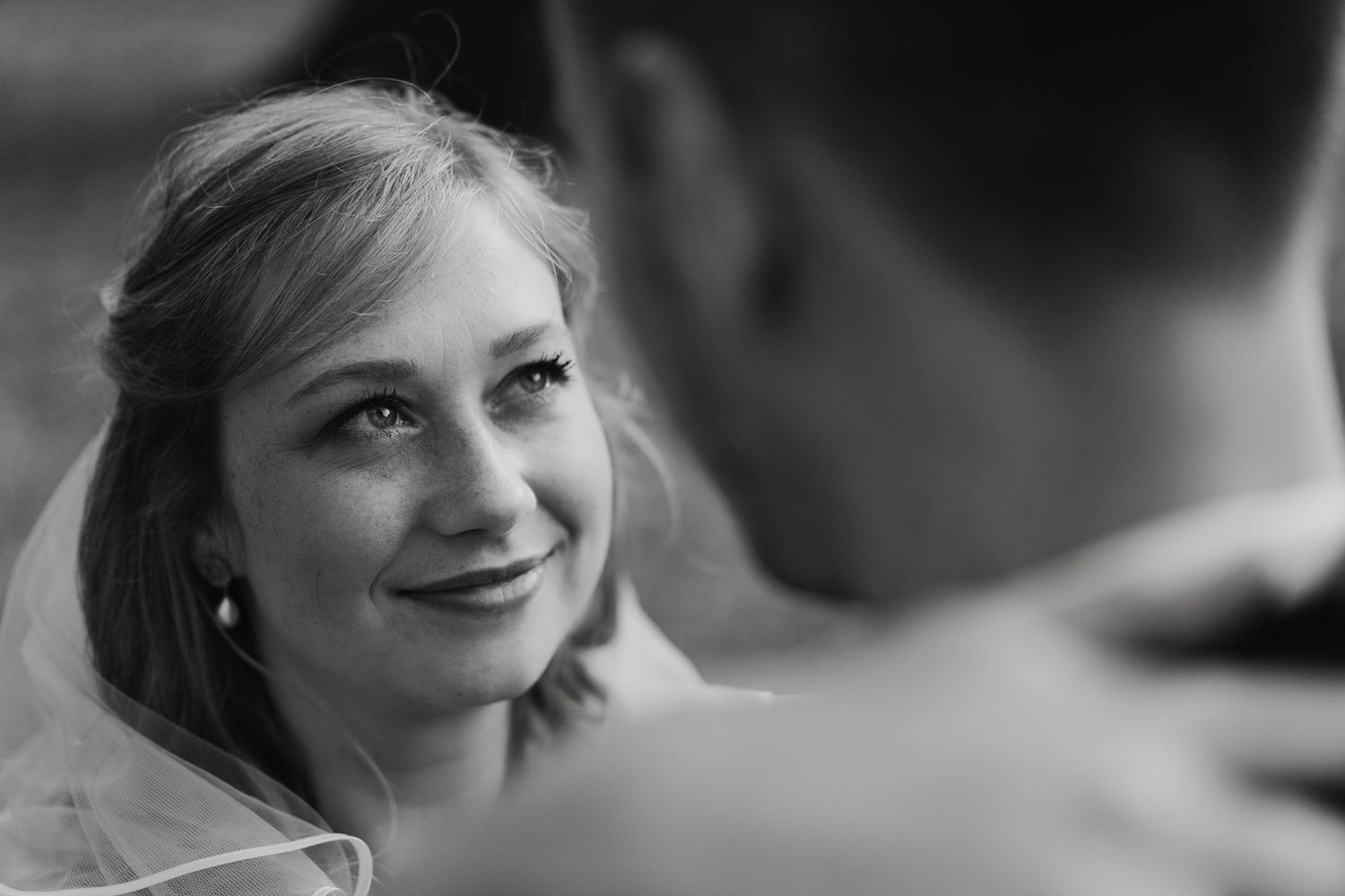 Black and white close-up of emotional bride smiling with tears during wedding ceremony.