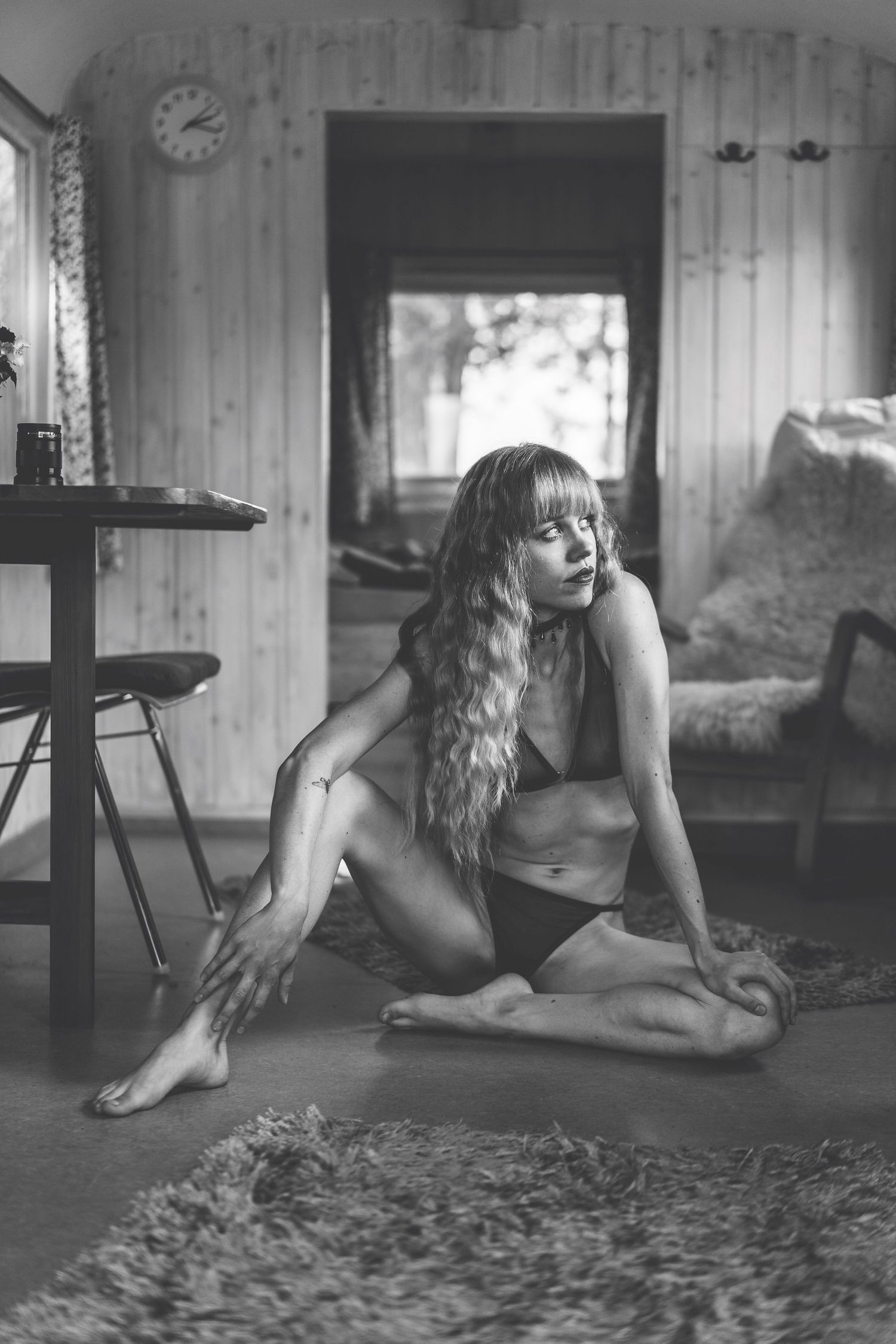 Black and white photo of a woman in bikini sitting on a rug inside a cozy vintage trailer home.