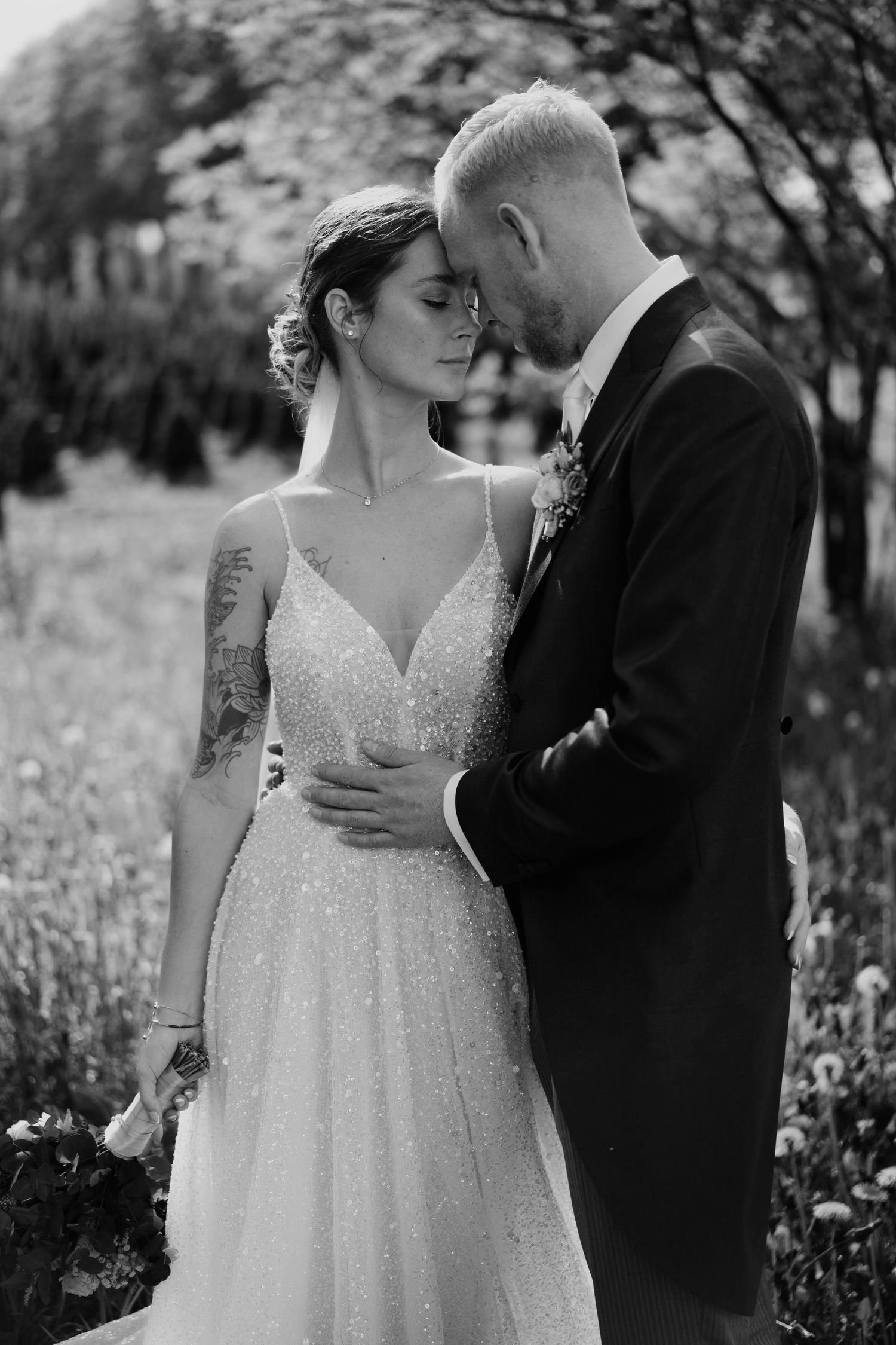 Black and white portrait of bride and groom sharing intimate moment in garden setting.