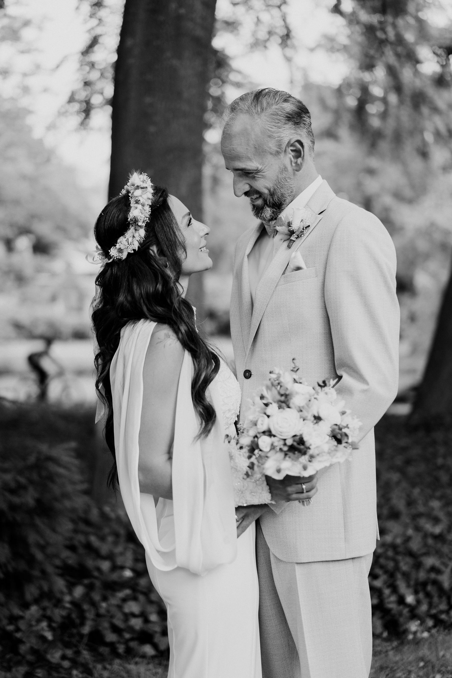 Black and white portrait of older groom in cream suit holding bouquet with dark-haired bride.