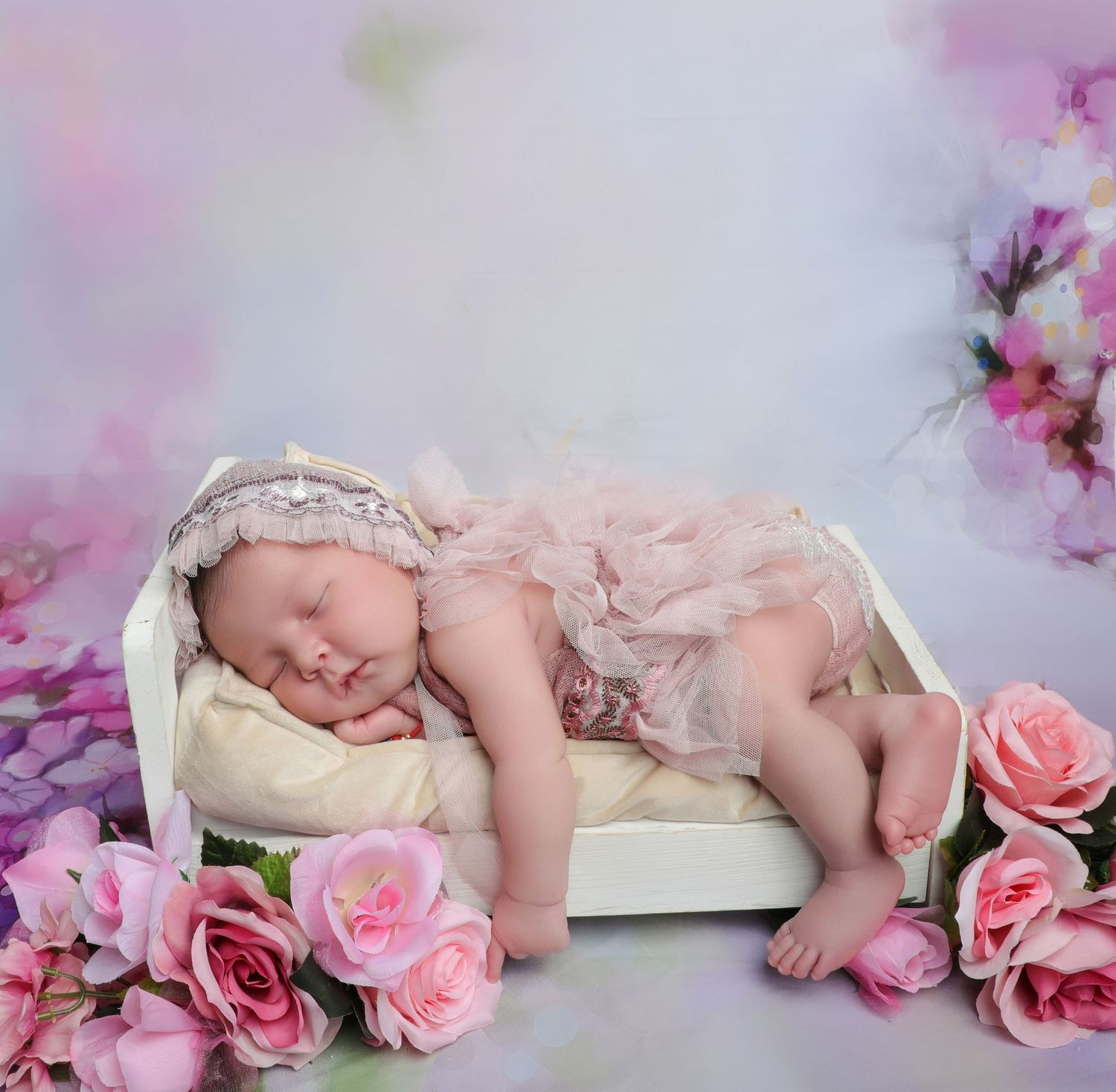 Sleeping newborn baby girl in pink lace outfit and headband resting in white mini bed surrounded by pink roses.