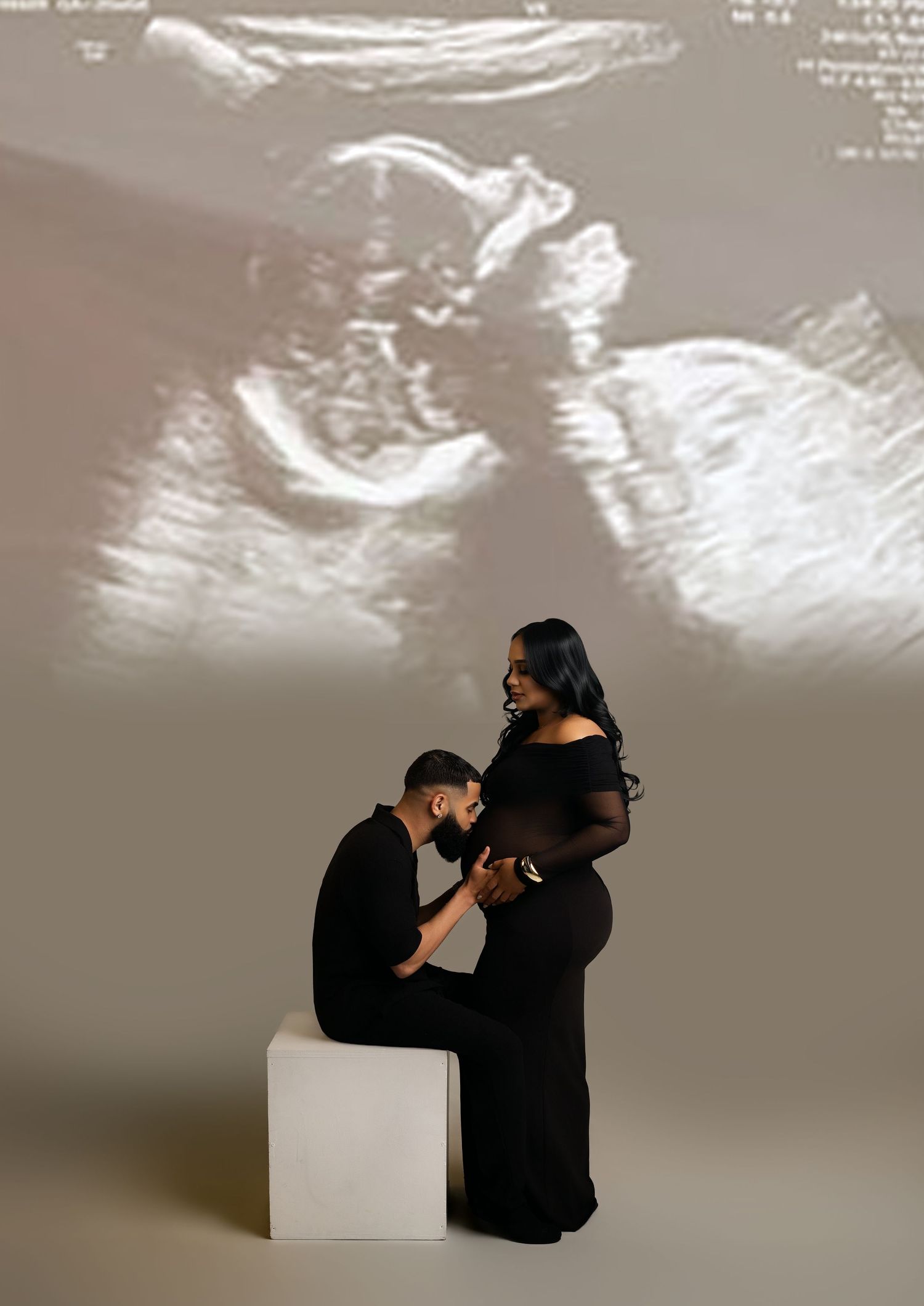 Couple in black outfits poses for maternity photo with ultrasound image projected behind them.