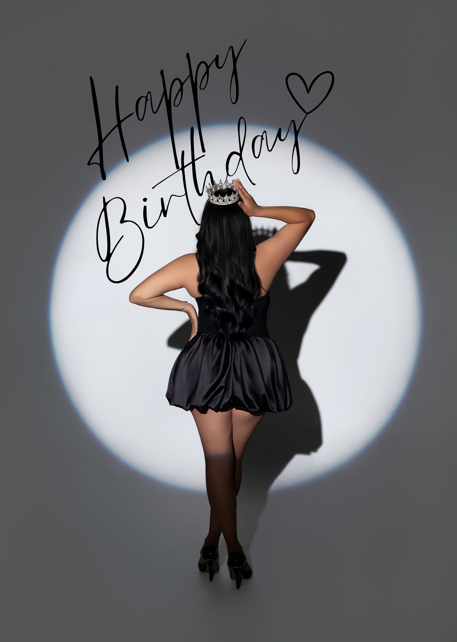 Illustrated woman in black mini dress and tiara poses in spotlight with Happy Birthday text overhead.