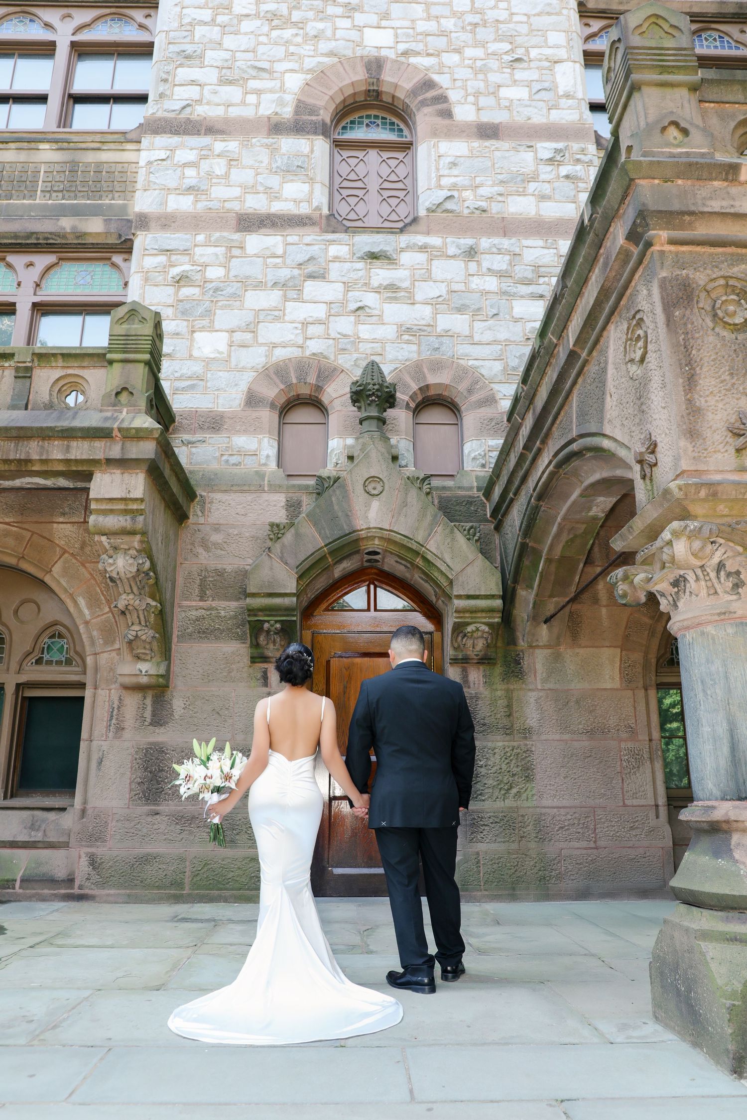 Bride and groom walking hand-in-hand toward ornate stone church entrance on their wedding day.