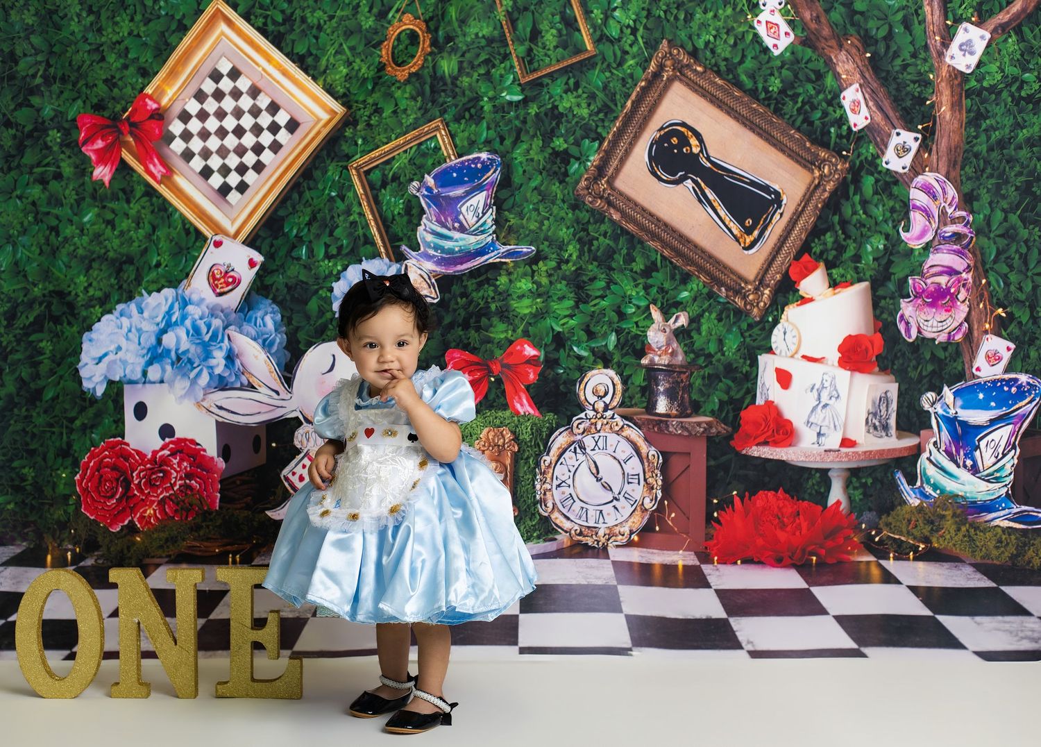 Baby girl in blue dress at Alice in Wonderland first birthday party with ONE sign and themed decorations.