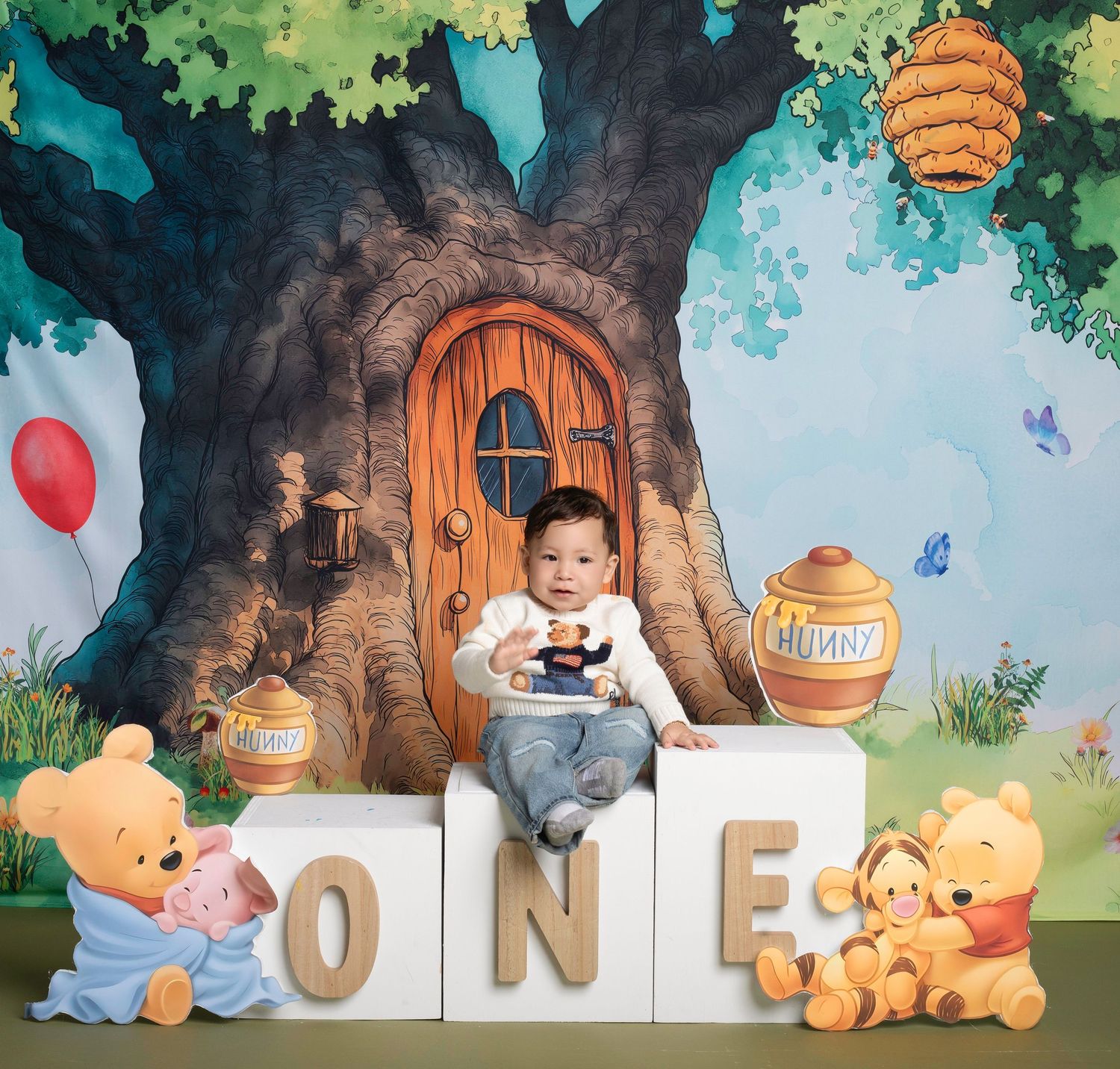 Baby's first birthday photo with Winnie the Pooh theme, sitting on ONE blocks in front of a magical tree backdrop.
