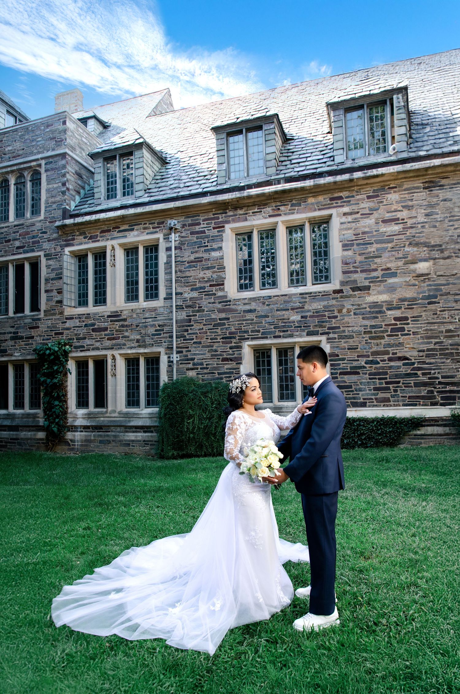Bride and groom share a romantic moment on green lawn before a grand stone manor on their wedding day.