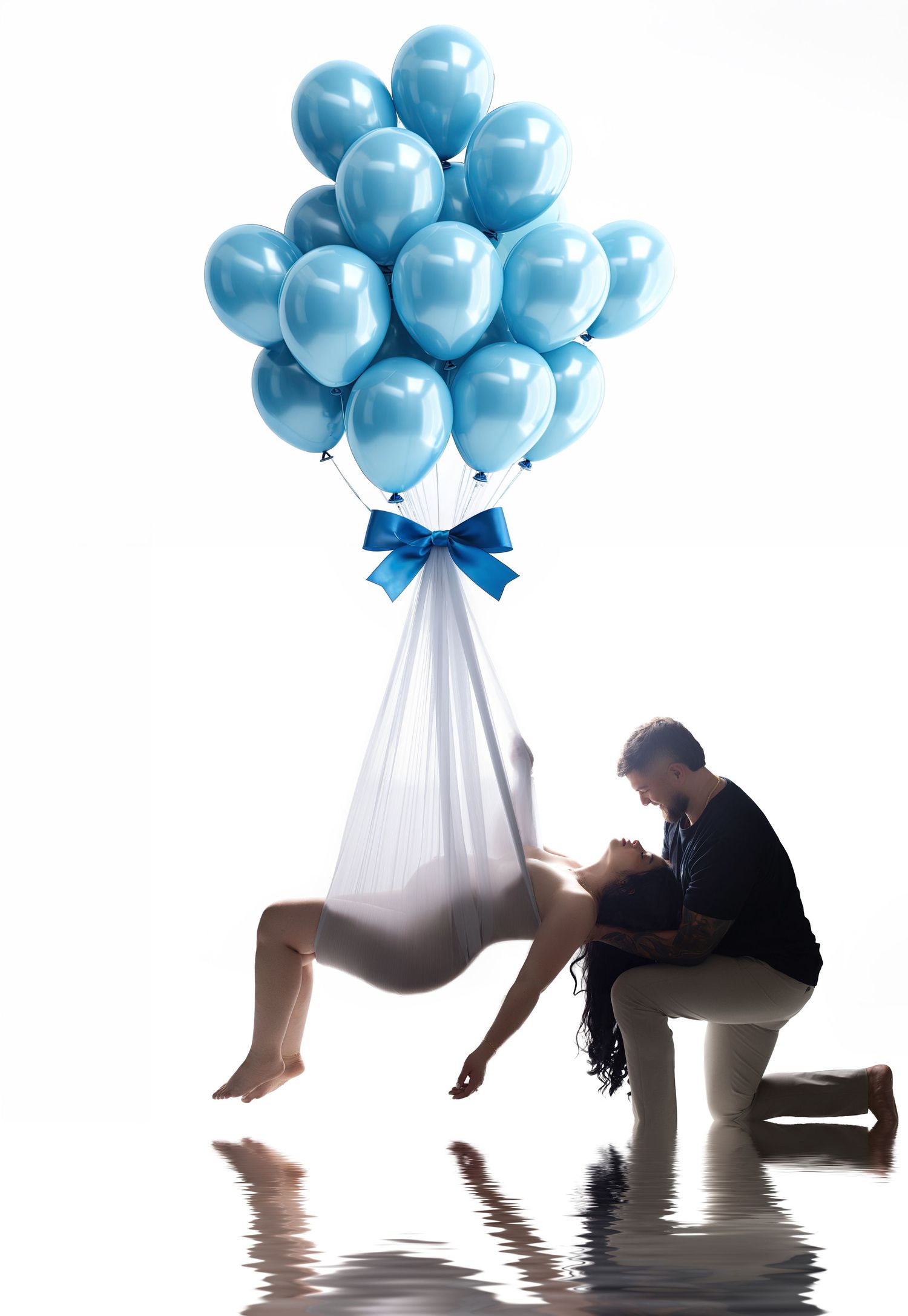 Pregnant woman suspended by blue balloons with bow, partner kneeling beside her, reflected on water surface.