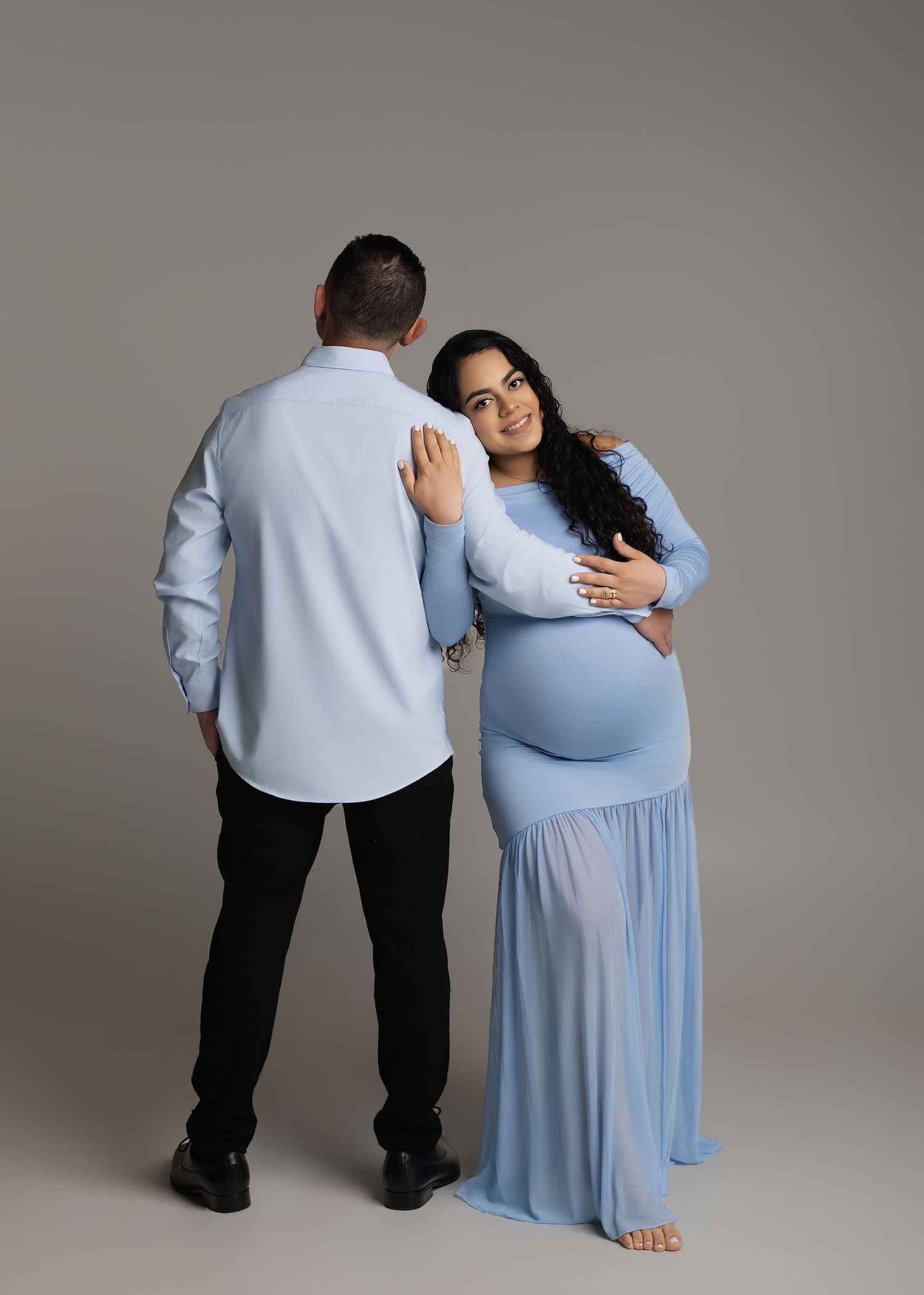 Pregnant woman in blue gown poses with partner in matching blue shirt during maternity photo session.