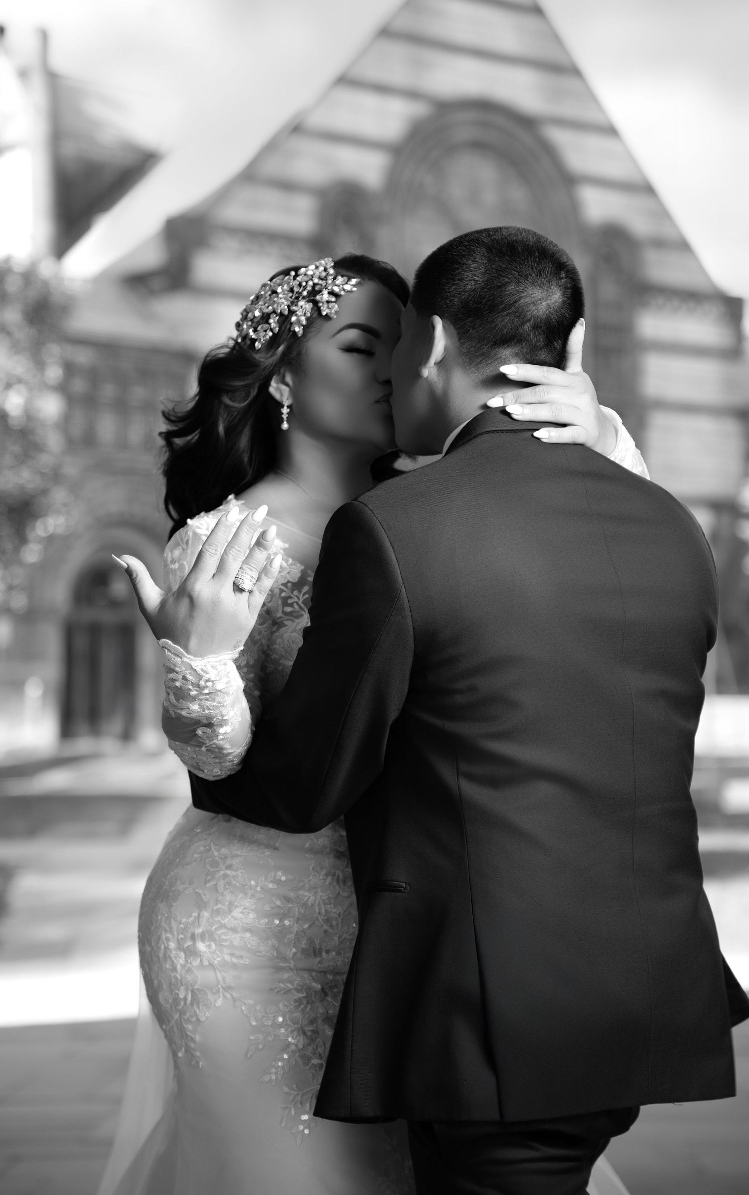 Black and white wedding photo of bride and groom kissing outside a church, bride wearing lace gown and floral tiara.