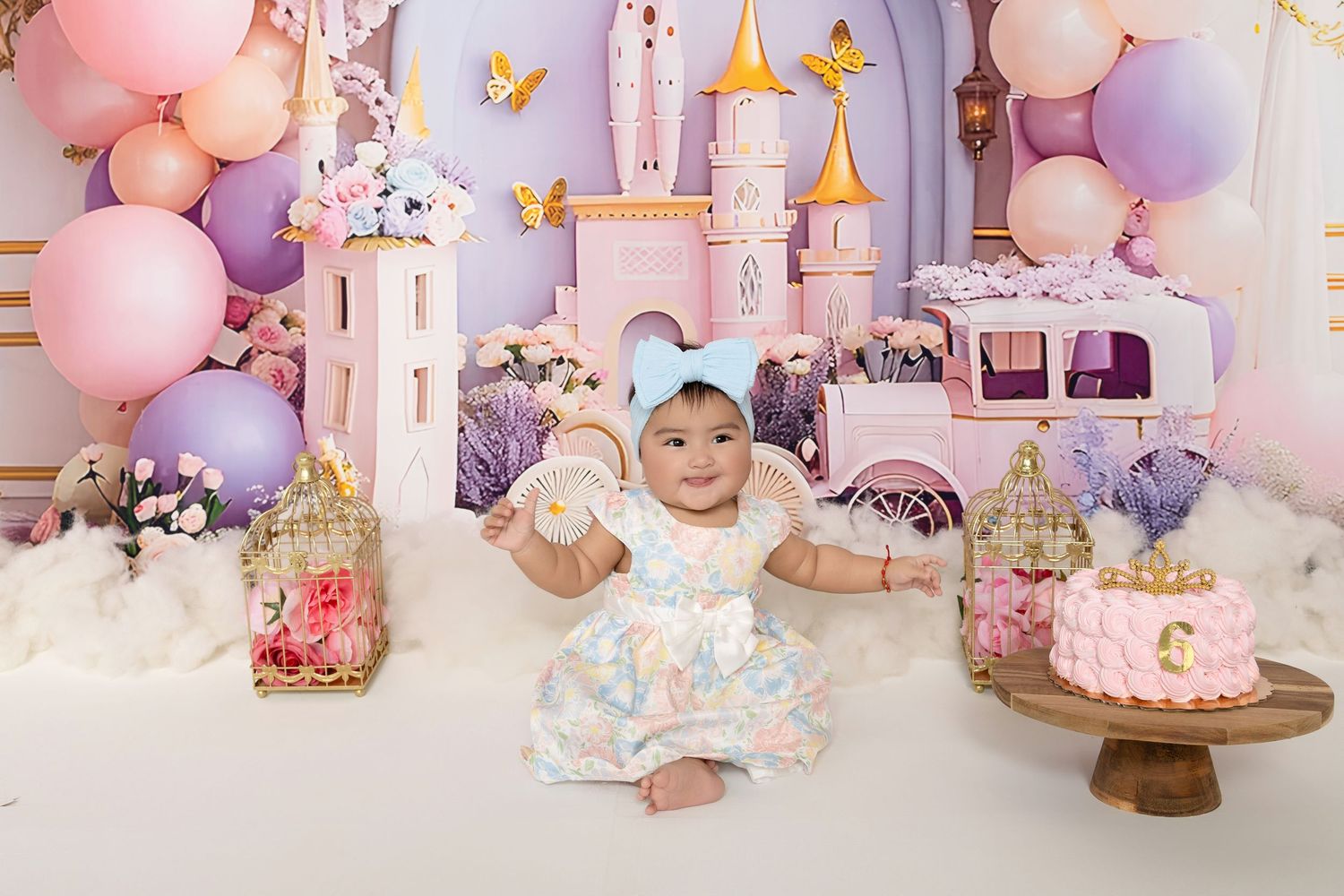 Baby girl in floral dress celebrates first birthday with princess castle backdrop, pink balloons, and smash cake.