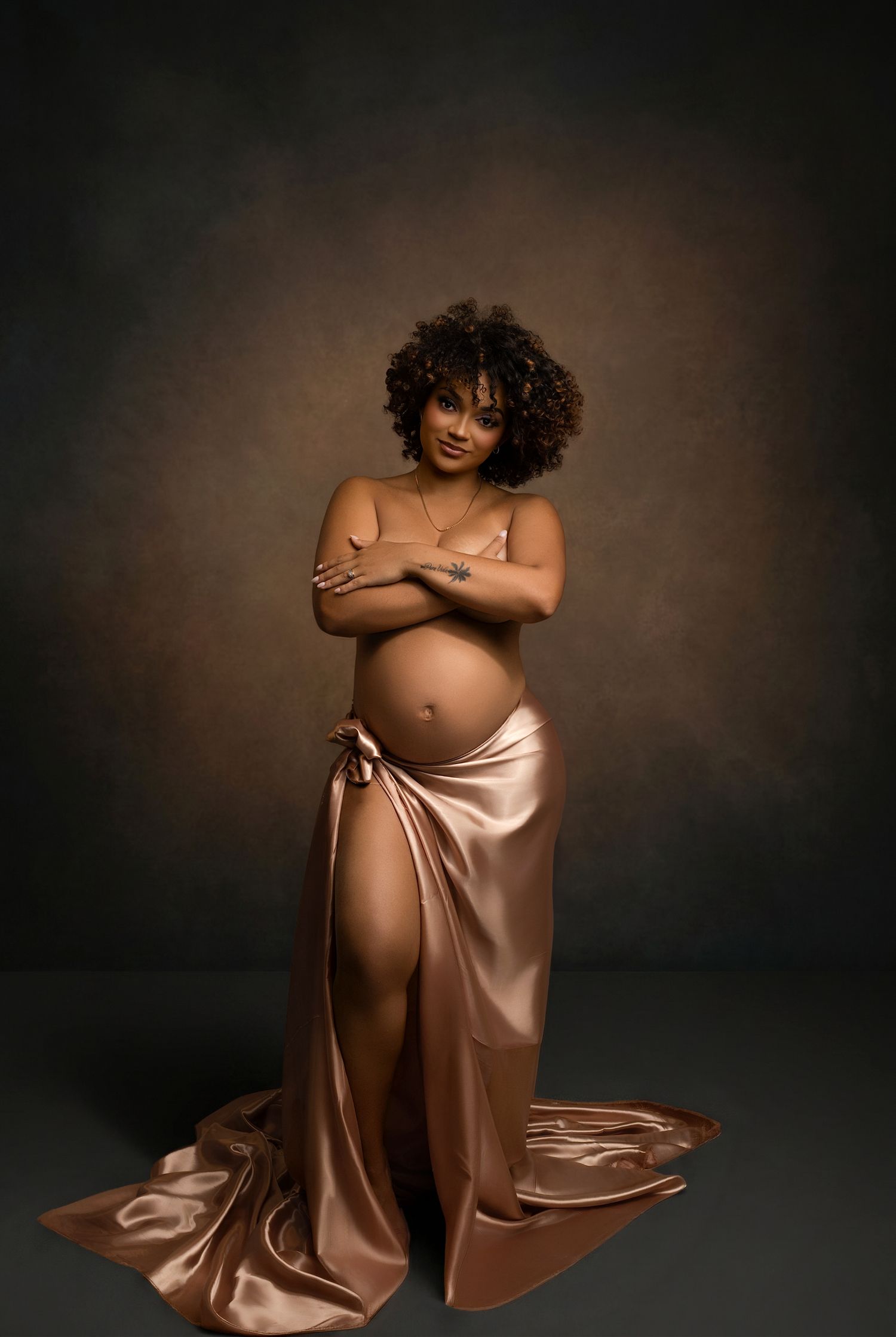 Pregnant woman in elegant rose gold satin wrap skirt poses confidently in a professional maternity photography studio.