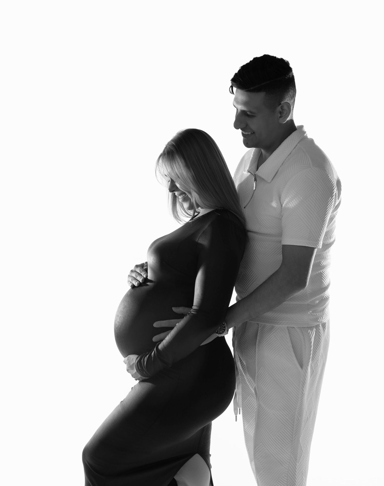 Black and white maternity photo of a pregnant woman in a black dress with her partner in white, both cradling her baby bump.