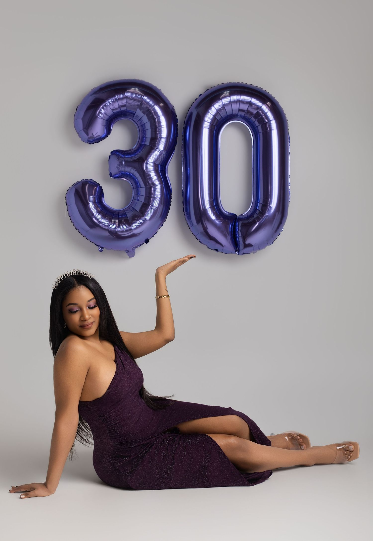 Woman in purple dress poses with large purple number 30 balloons, celebrating her 30th birthday milestone.