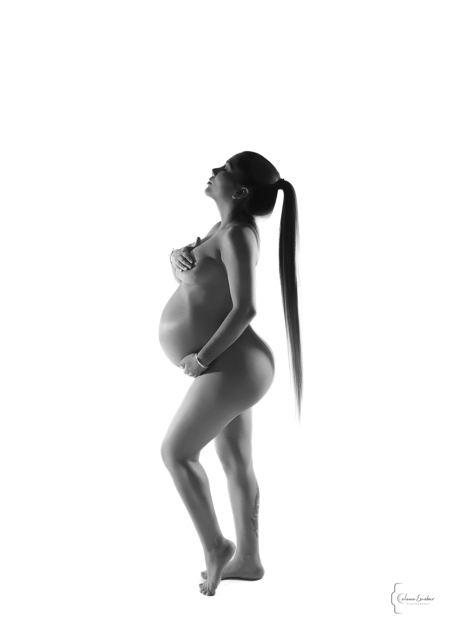 Black and white silhouette of a pregnant woman cradling her baby bump, posing gracefully with a long ponytail.
