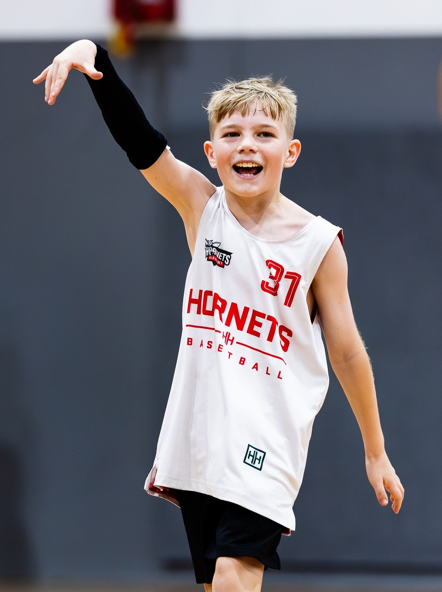 Young boy in Hornets Basketball jersey number 37 celebrating with arm raised during youth basketball game.