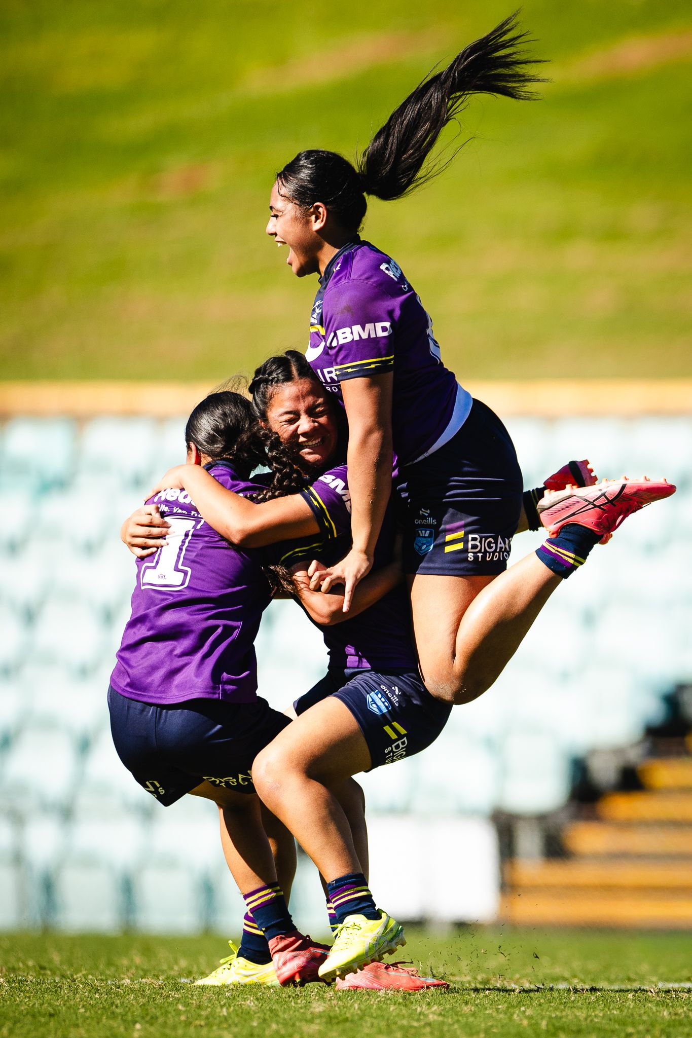 Women rugby league players in purple jerseys celebrate a try, with one player leaping joyfully during a match.
