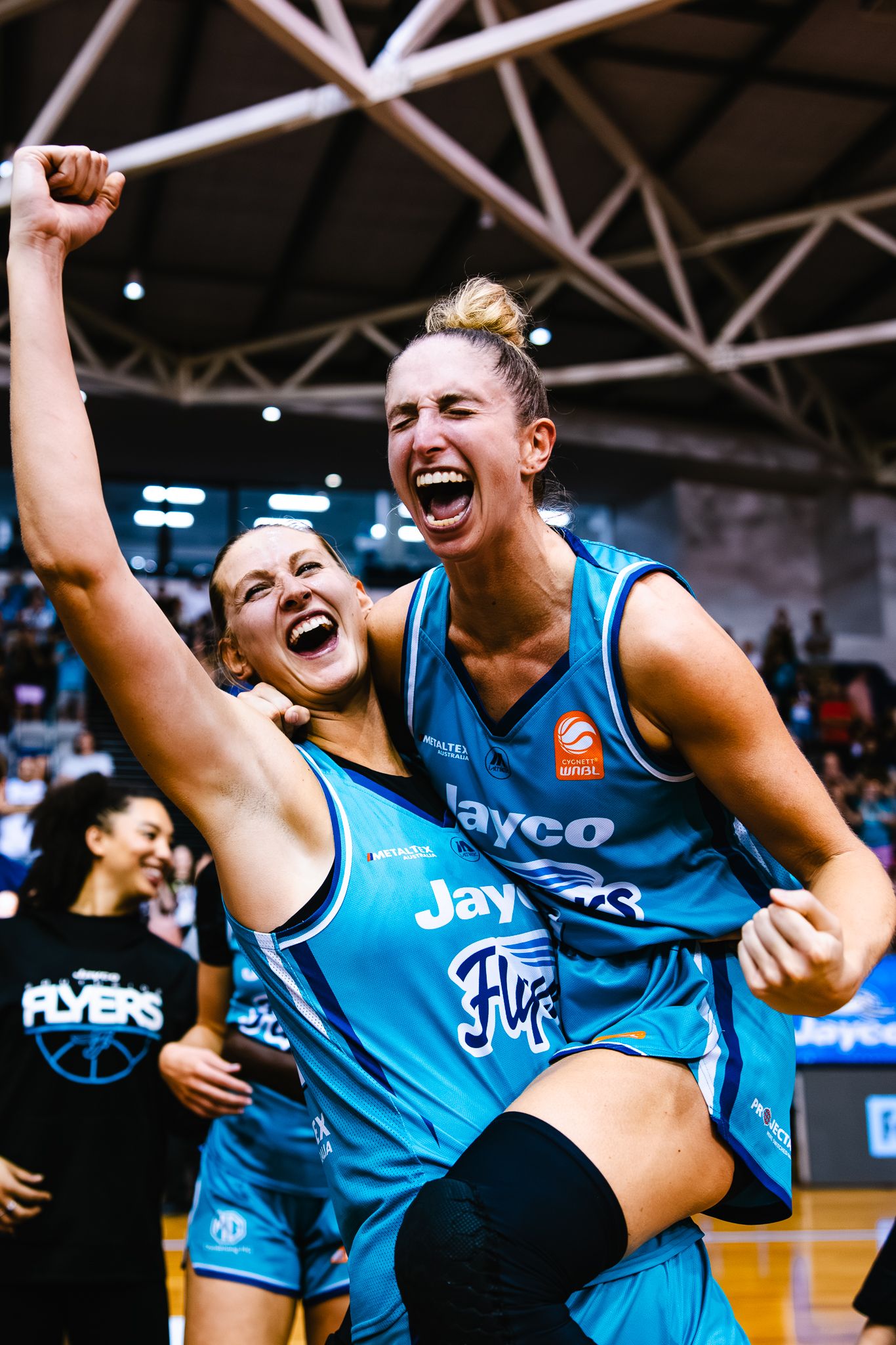 Basketball players in light blue jerseys celebrate enthusiastically on the court during a game.