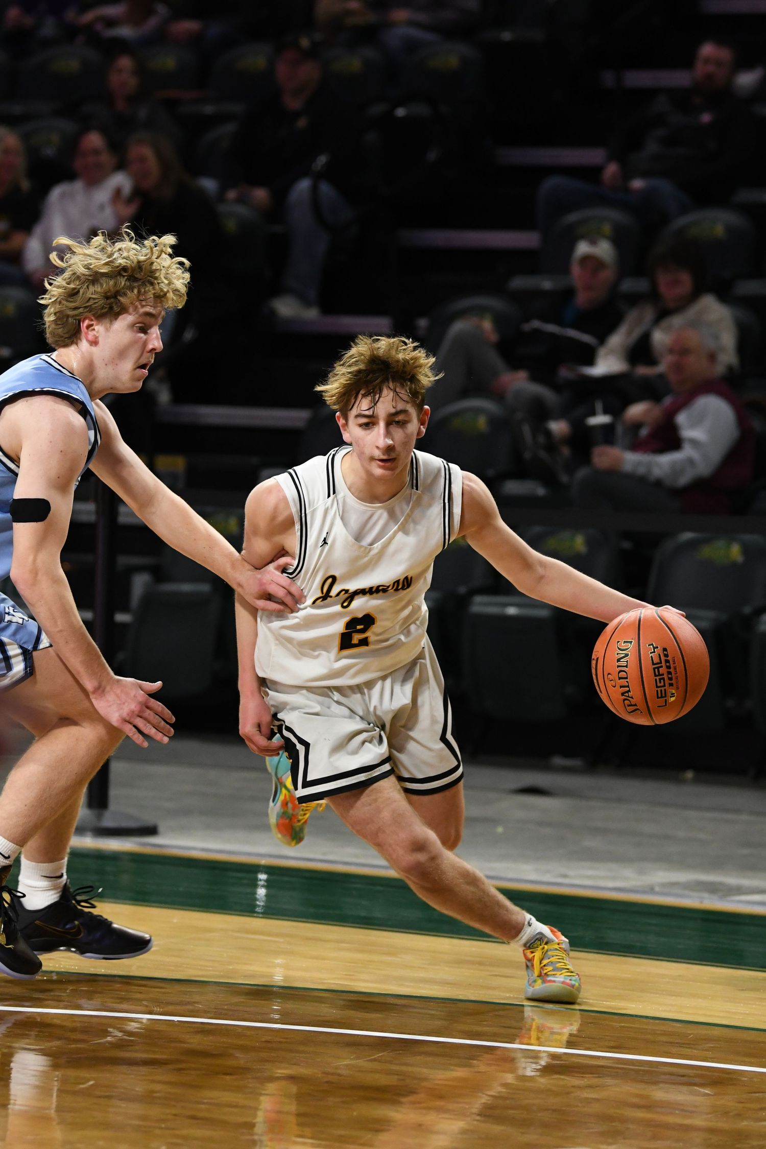 Basketball player drives past defender while dribbling on the hardwood court.