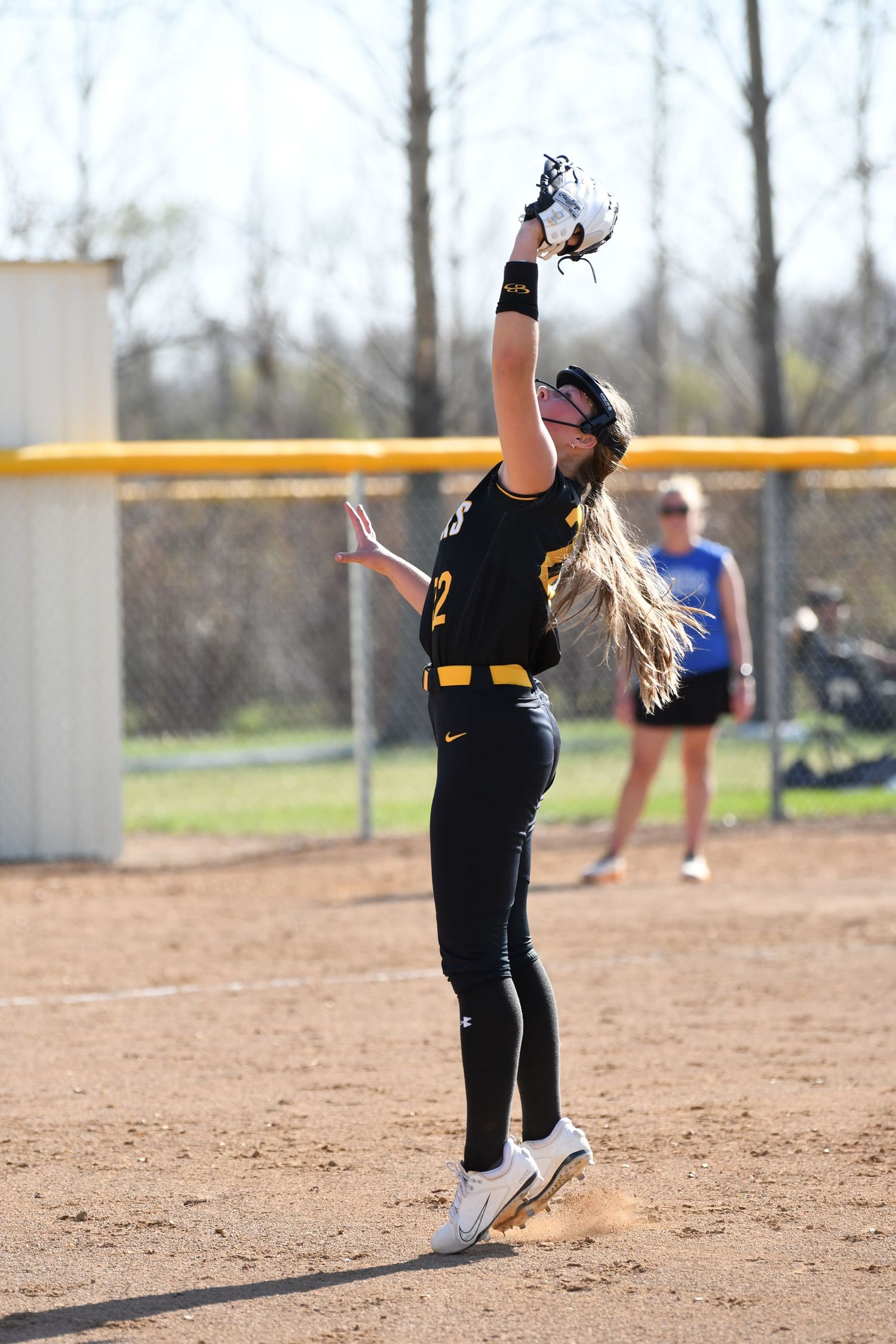 Female softball pitcher in black uniform winds up for pitch delivery on dirt mound.