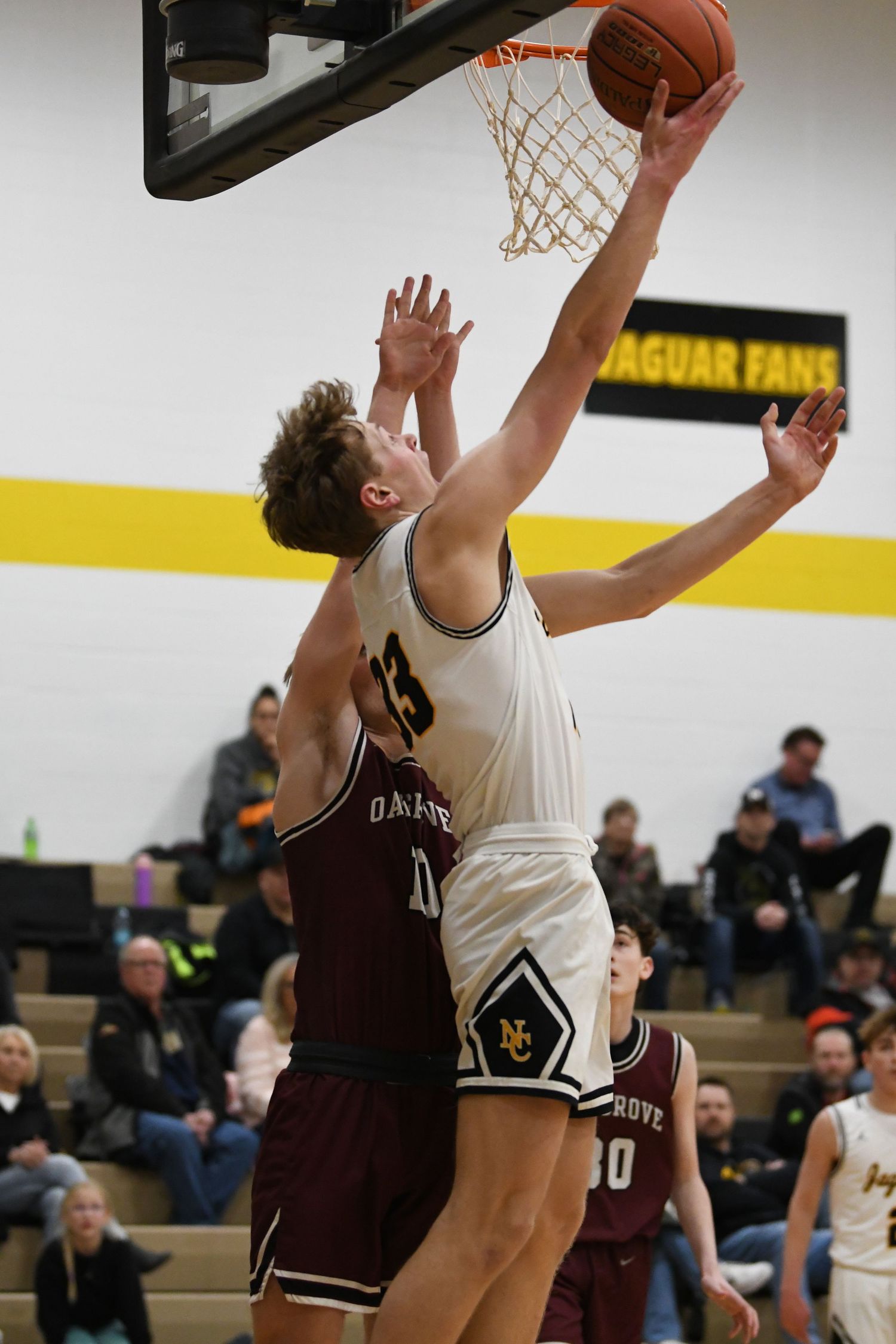 Basketball player in white uniform attempts a layup while being defended by player in maroon jersey.