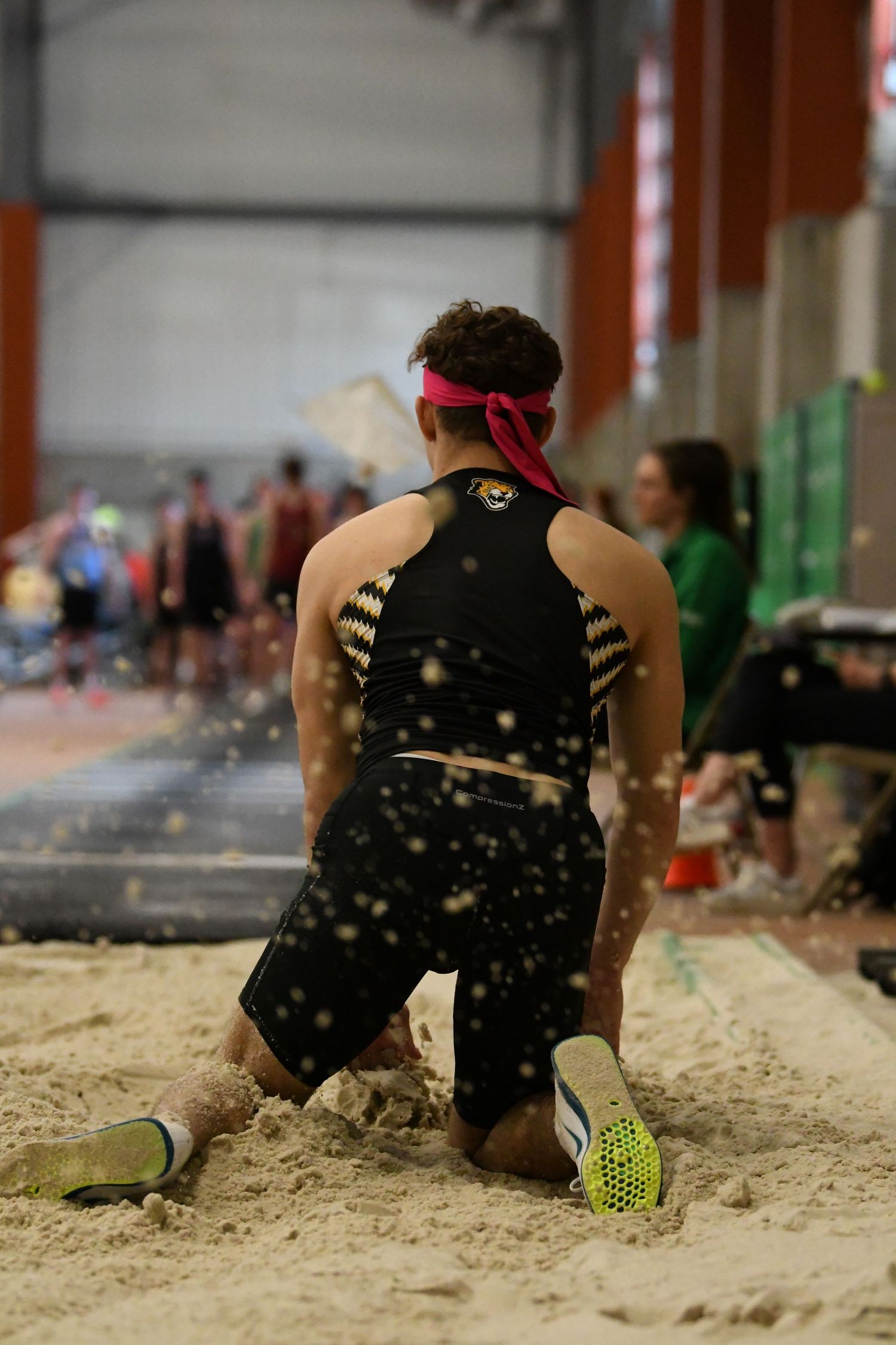 A long jumper creates splash of sand during indoor track meet landing.