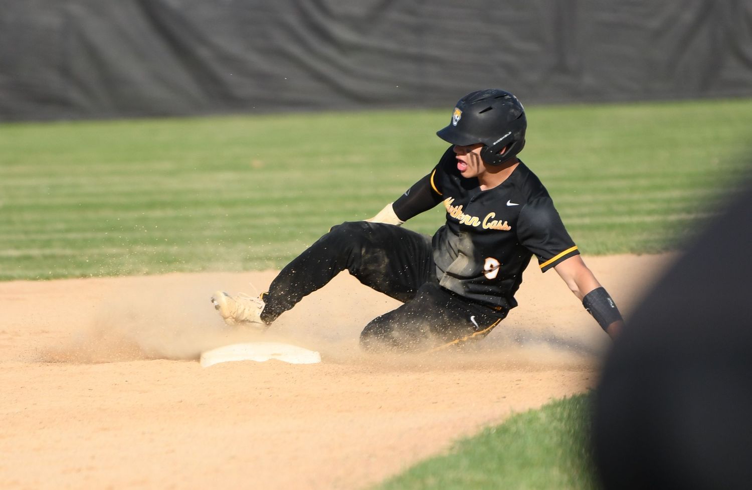 Baseball player slides into base creating dust cloud during intense game.