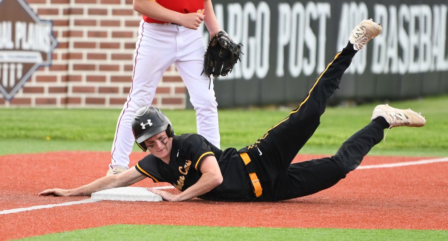 Baseball player sliding into base during an intense game play moment on red dirt field.
