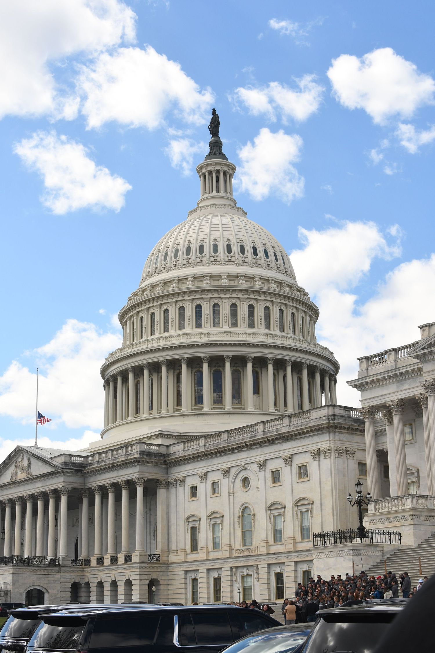 The US Capitol Building dome rises against a bright blue sky with puffy white clouds.