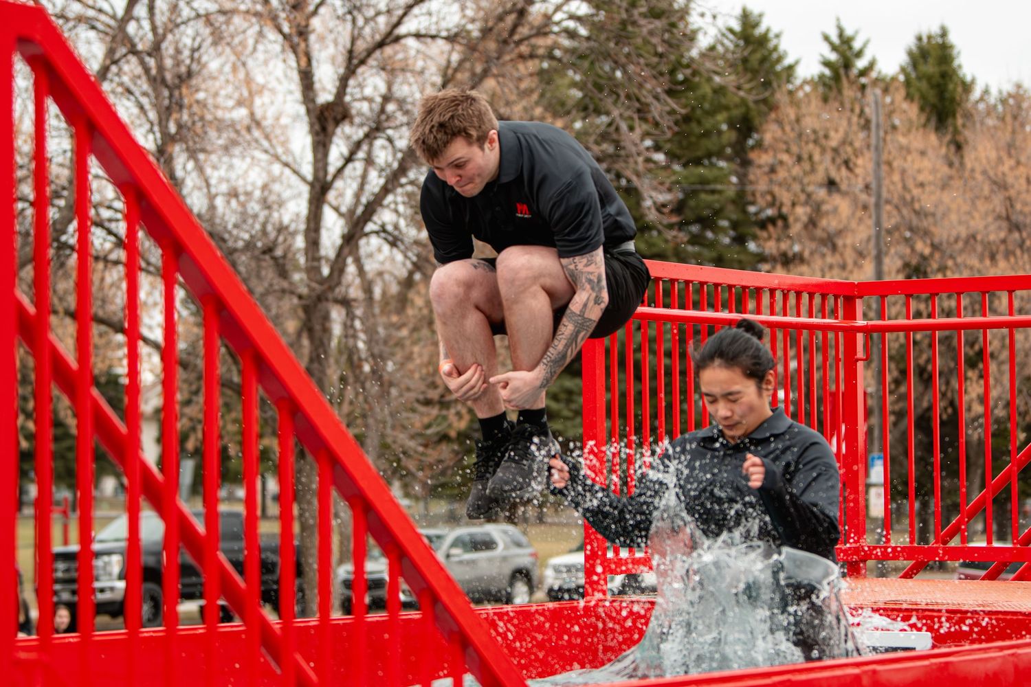Two people participate in a dunk tank challenge on a red structure outdoors, with one jumping in splash.