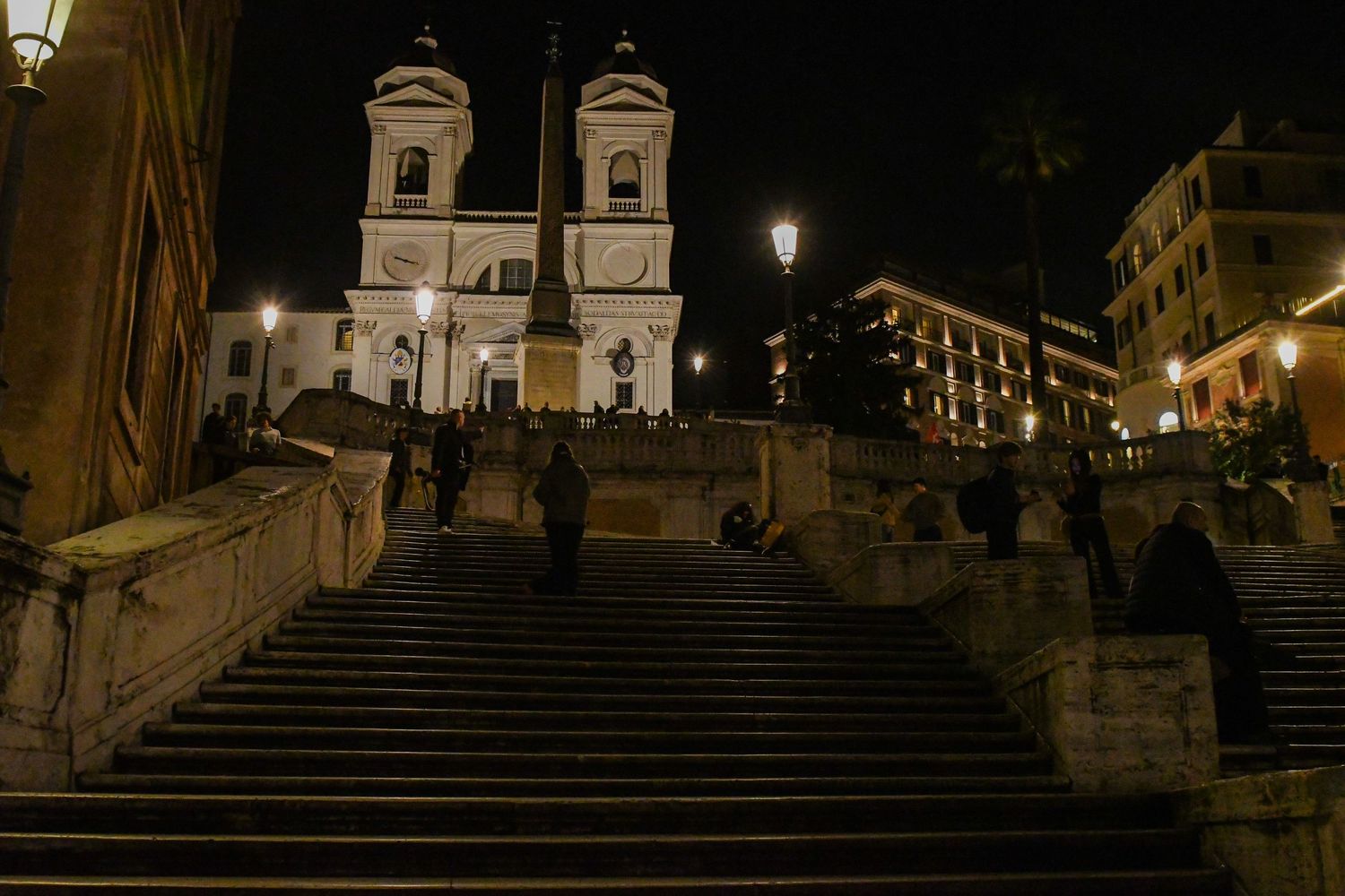 The Spanish Steps and Trinita dei Monti church illuminated at night in Rome, with visitors sitting on the iconic staircase.