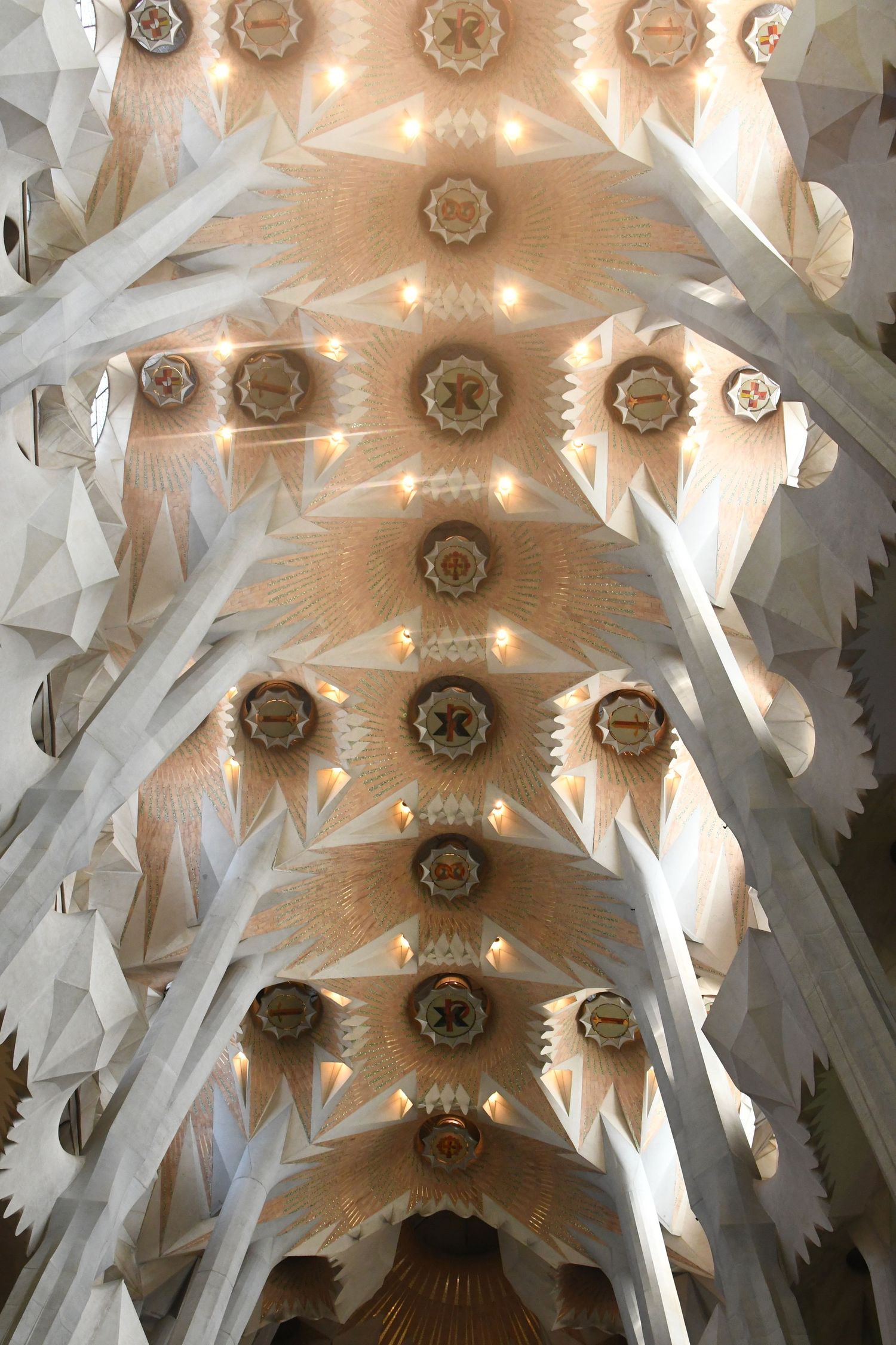 Stunning geometric ceiling architecture inside Sagrada Familia with white columns and golden lighting.