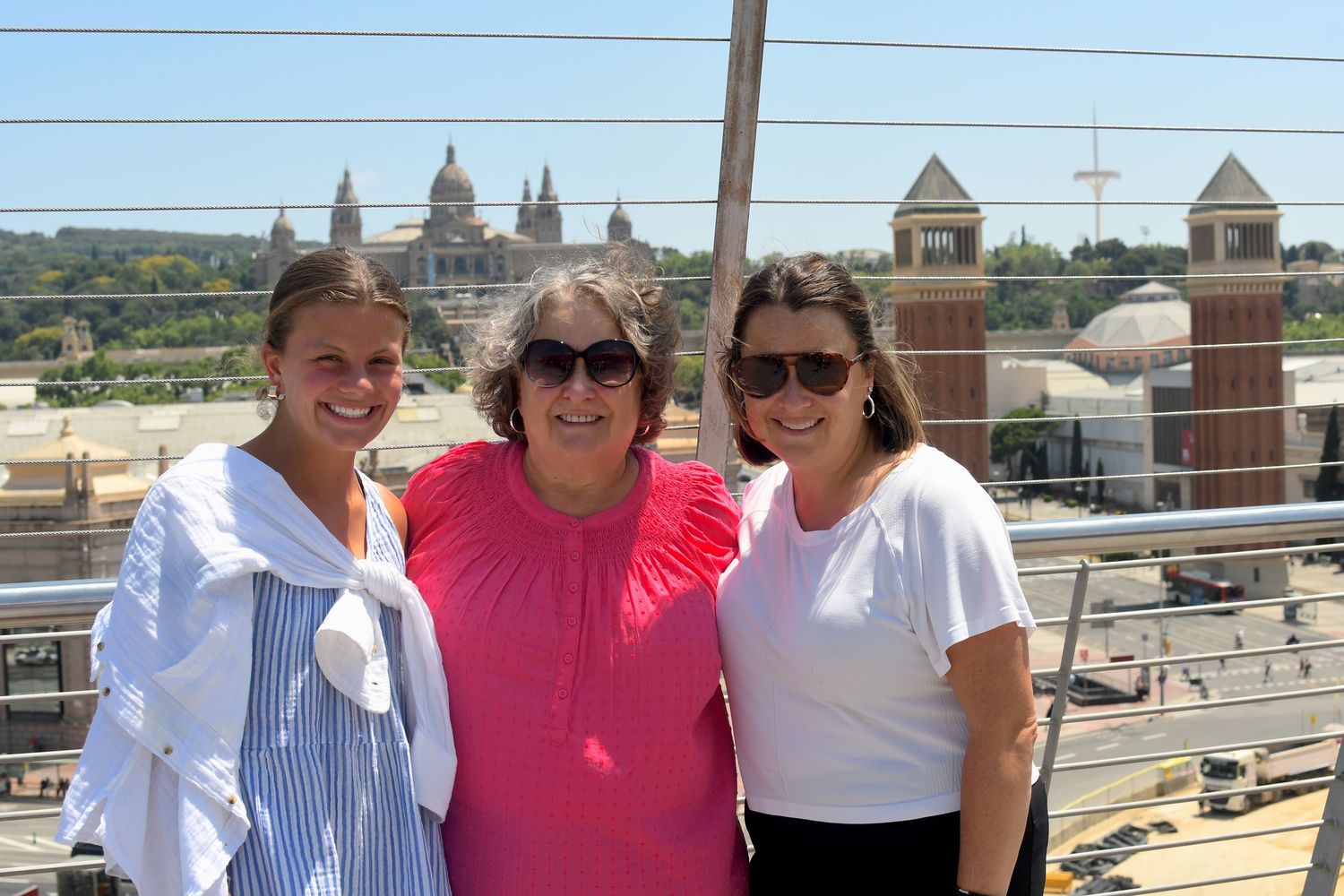 Three people pose on a balcony with historic architecture and power lines visible in the background.