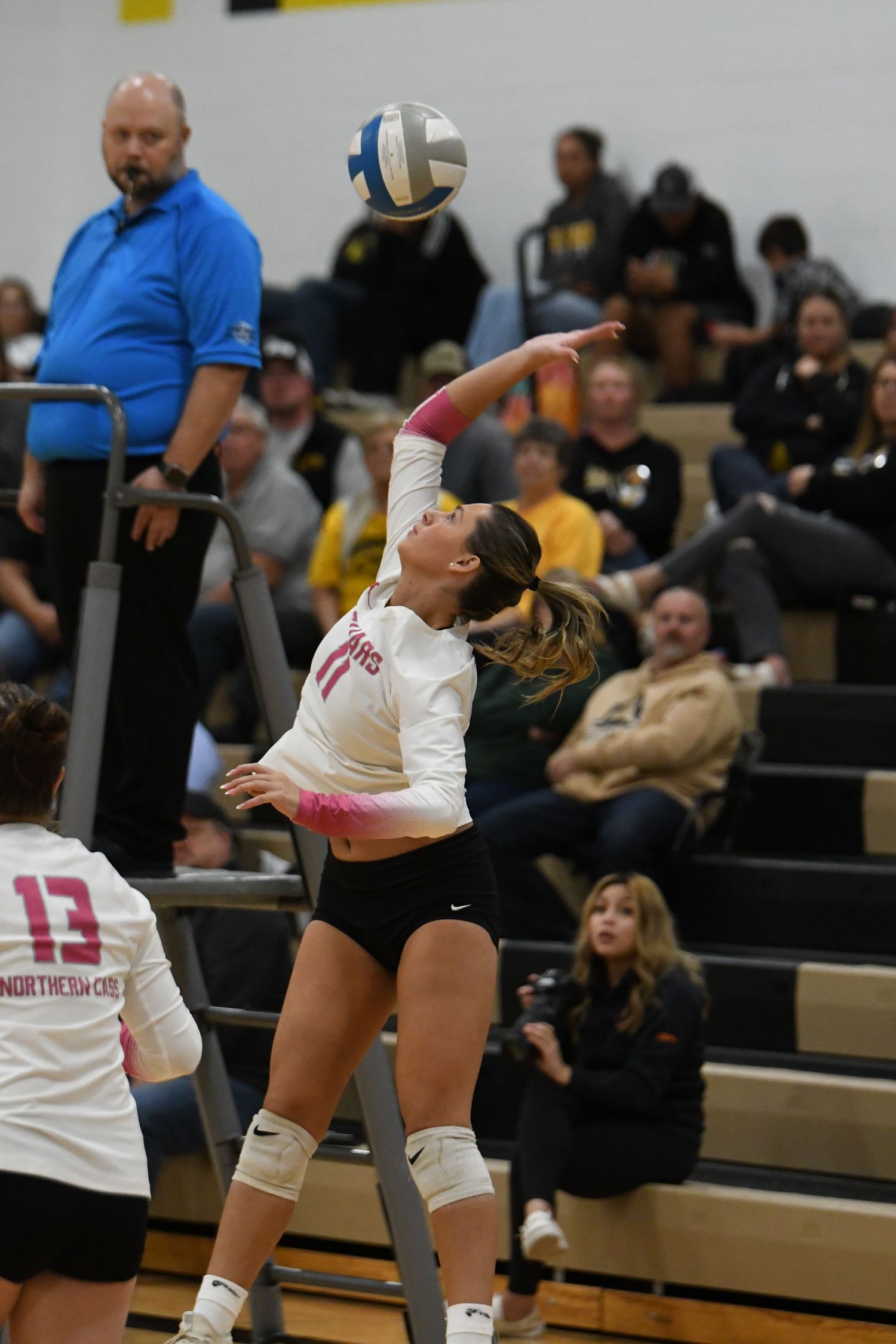 Two volleyball players leap high at the net during a competitive match in the gymnasium.