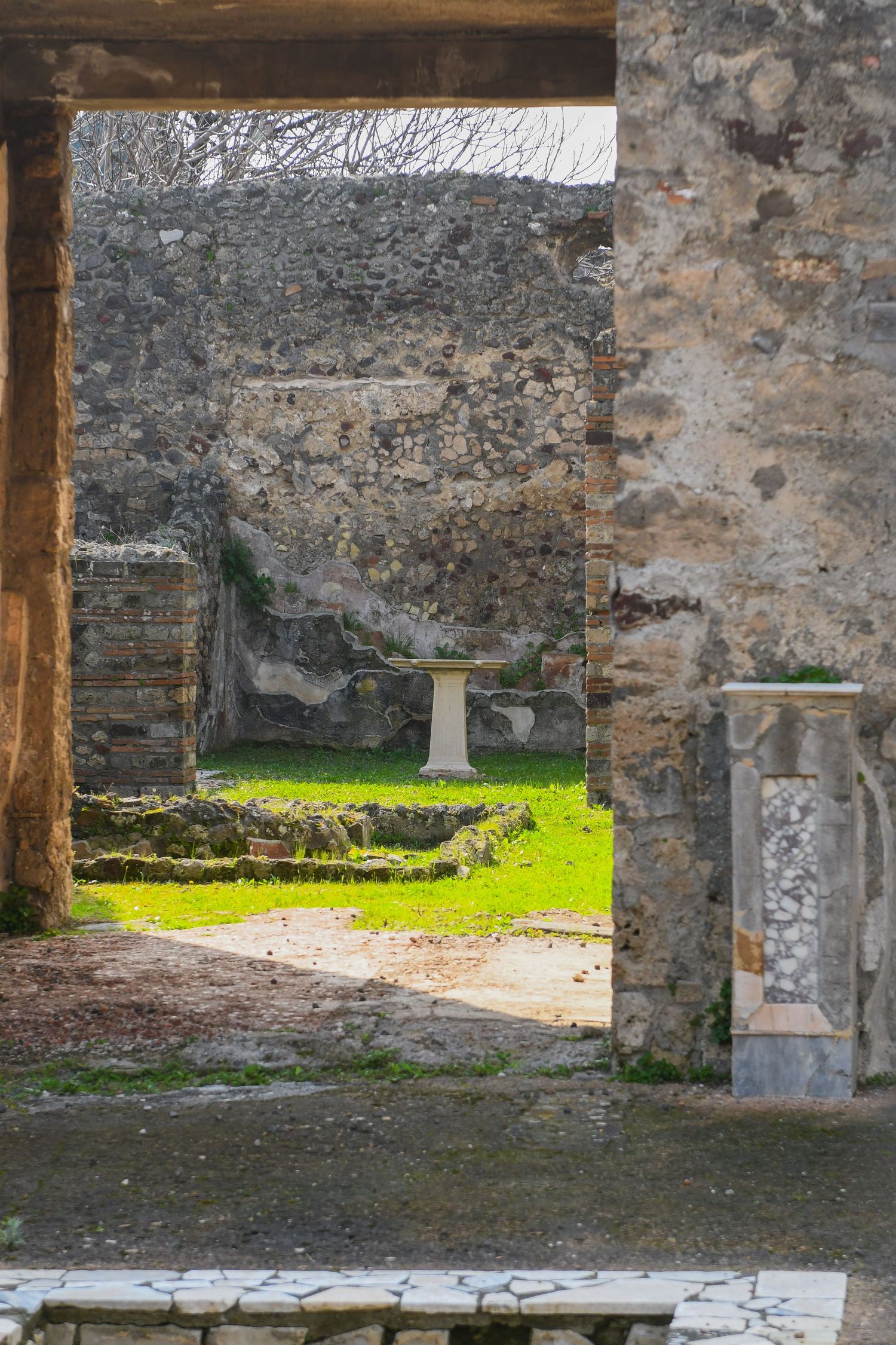 Ancient stone ruins with crumbling walls and columns reveal remnants of a historic structure against a grassy landscape.