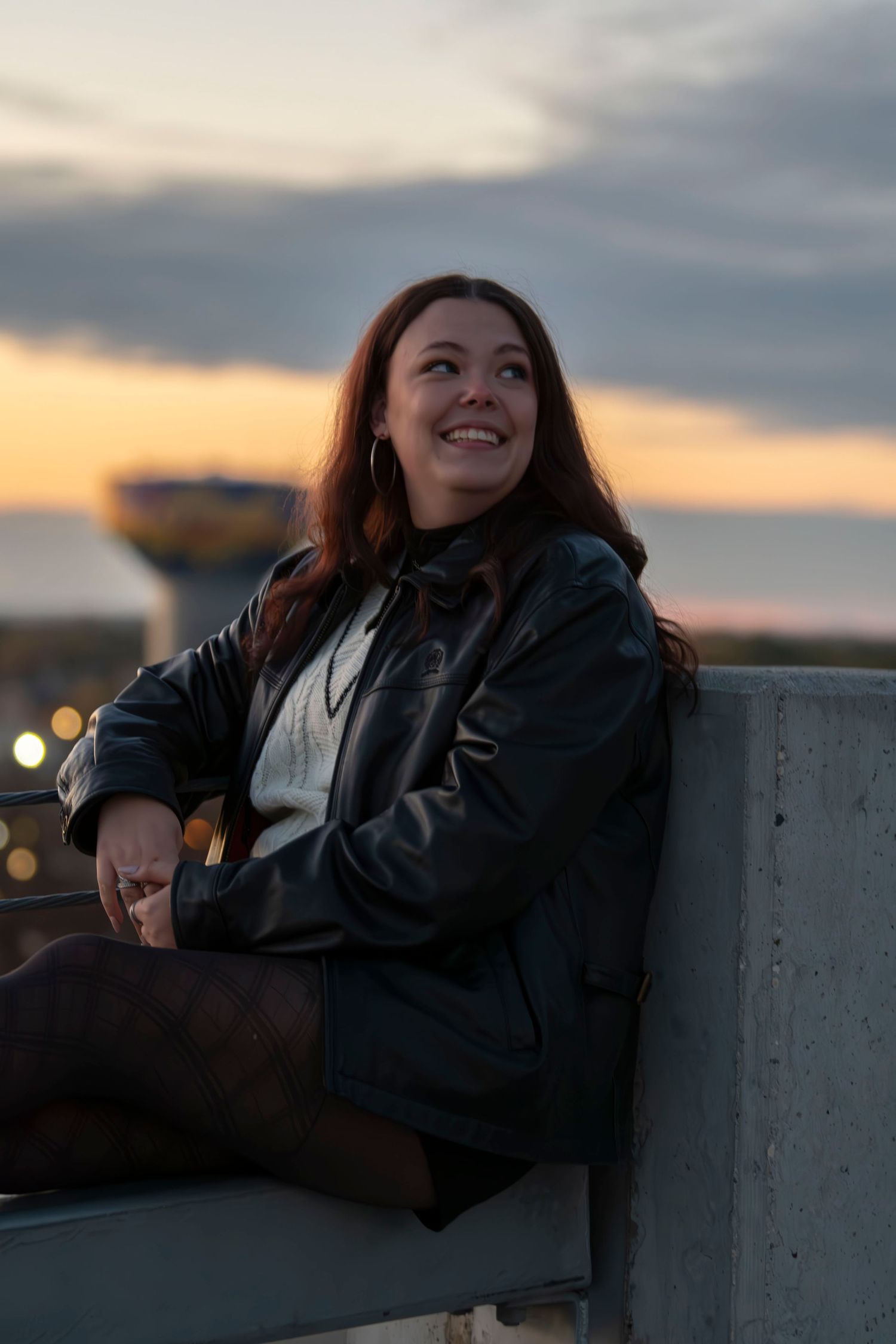 A sunset portrait with a leather jacket and white sweater against a warm evening sky.
