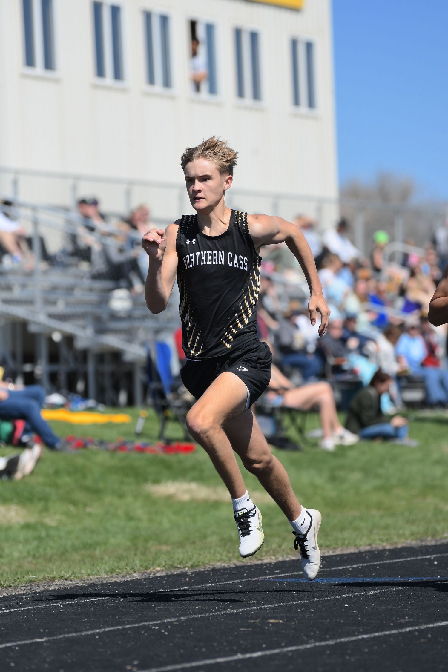 Runner in black Northern Cass uniform sprinting on outdoor track during competition.