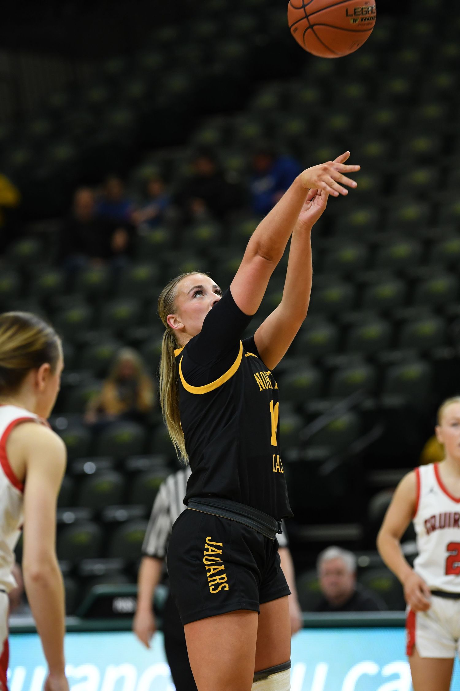 Basketball player in black and gold uniform takes a jump shot during competitive game.