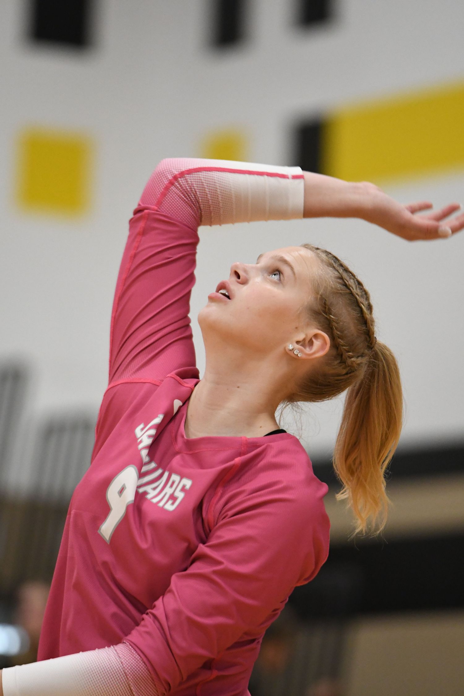 Volleyball player in pink jersey executes overhead serve during competitive match.