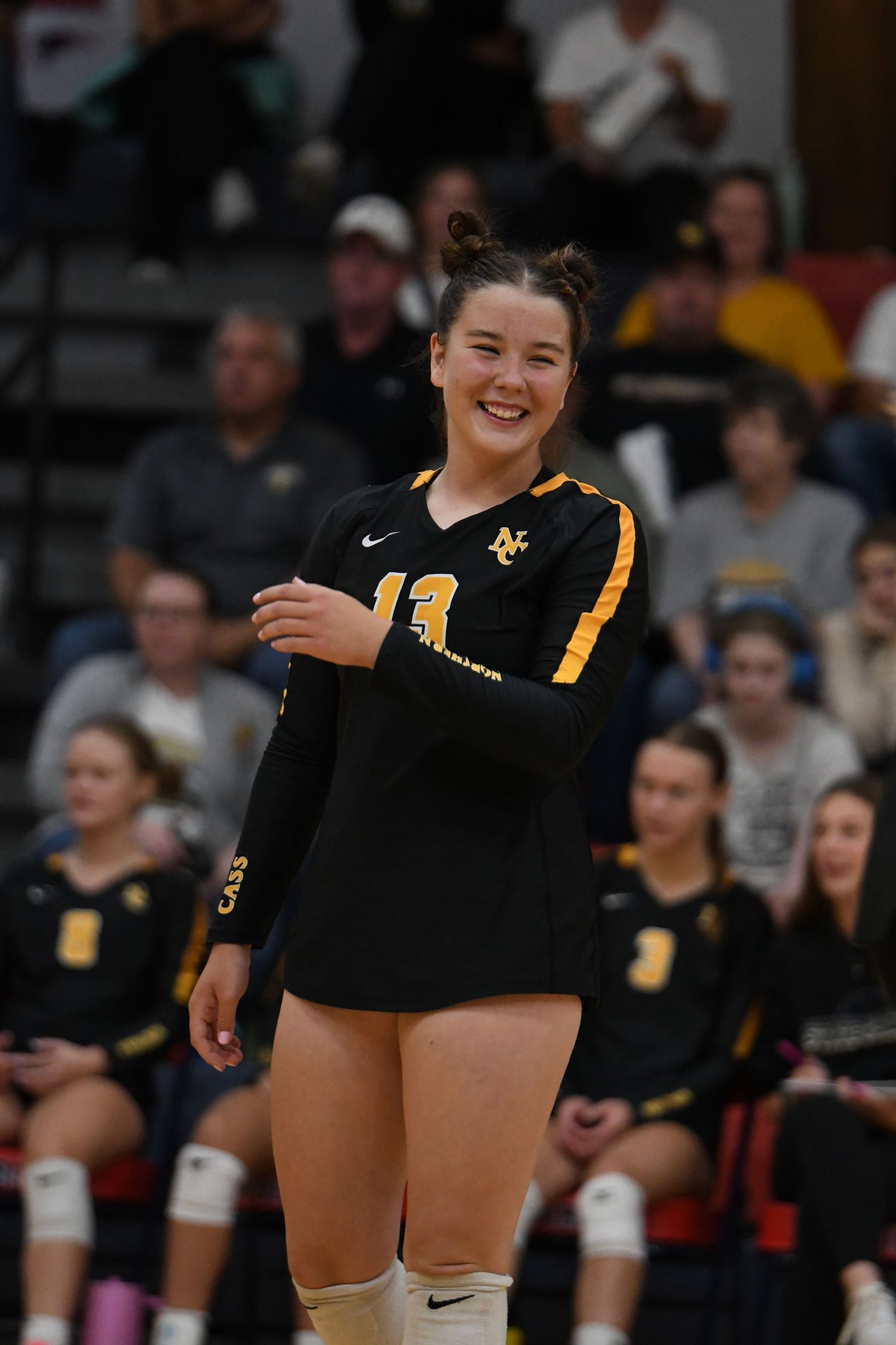 Volleyball player in black and yellow uniform smiles during a match.