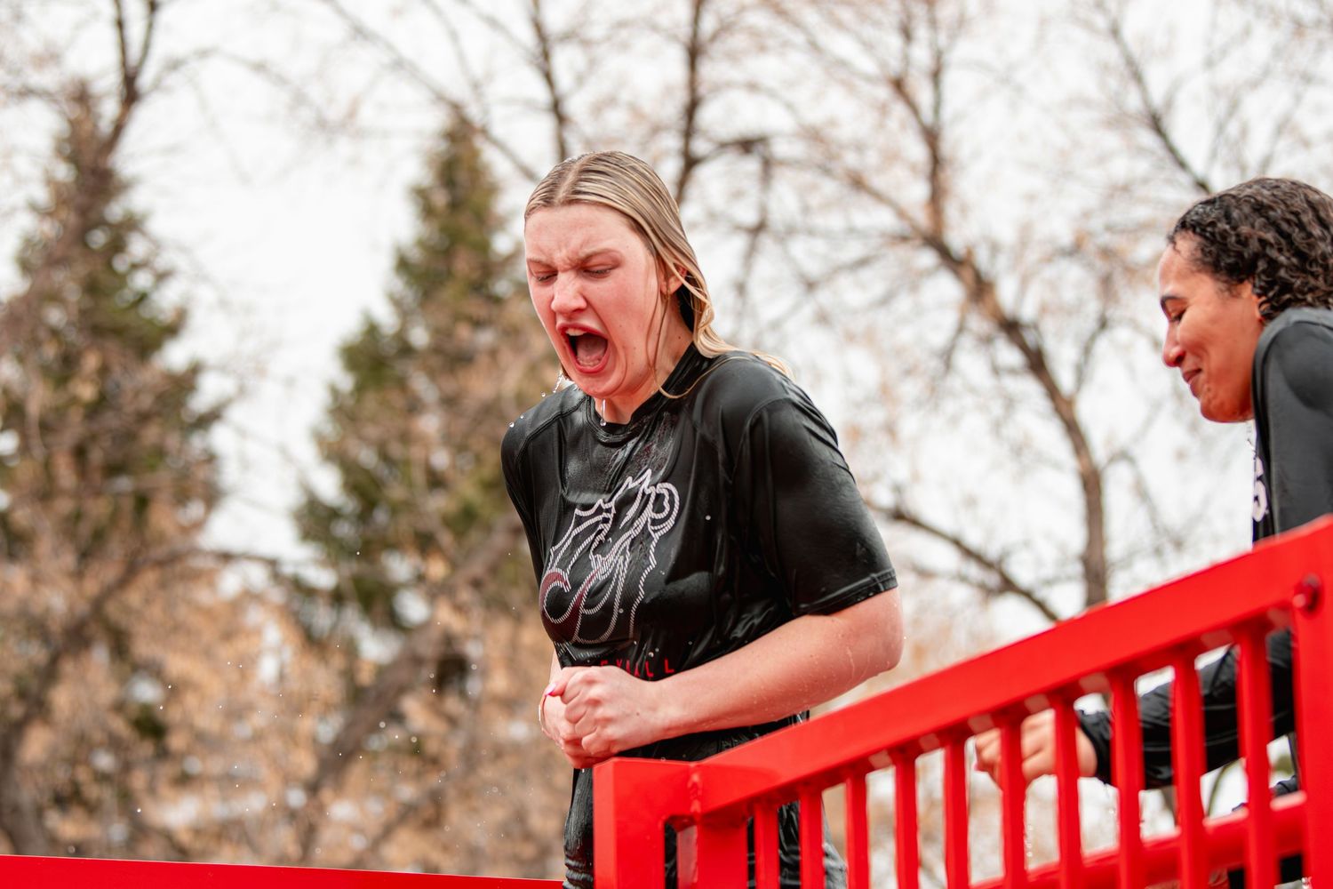 Excited young man yelling with mouth open, leaning on red railing outdoors during a lively event.