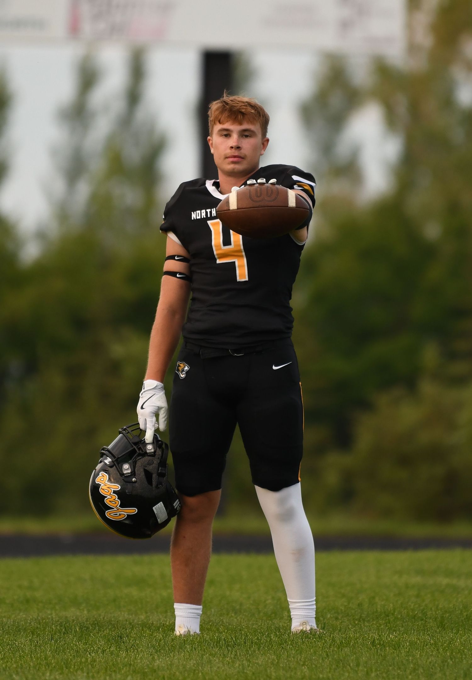 Football player in black uniform kneeling on grass field during outdoor practice or game.