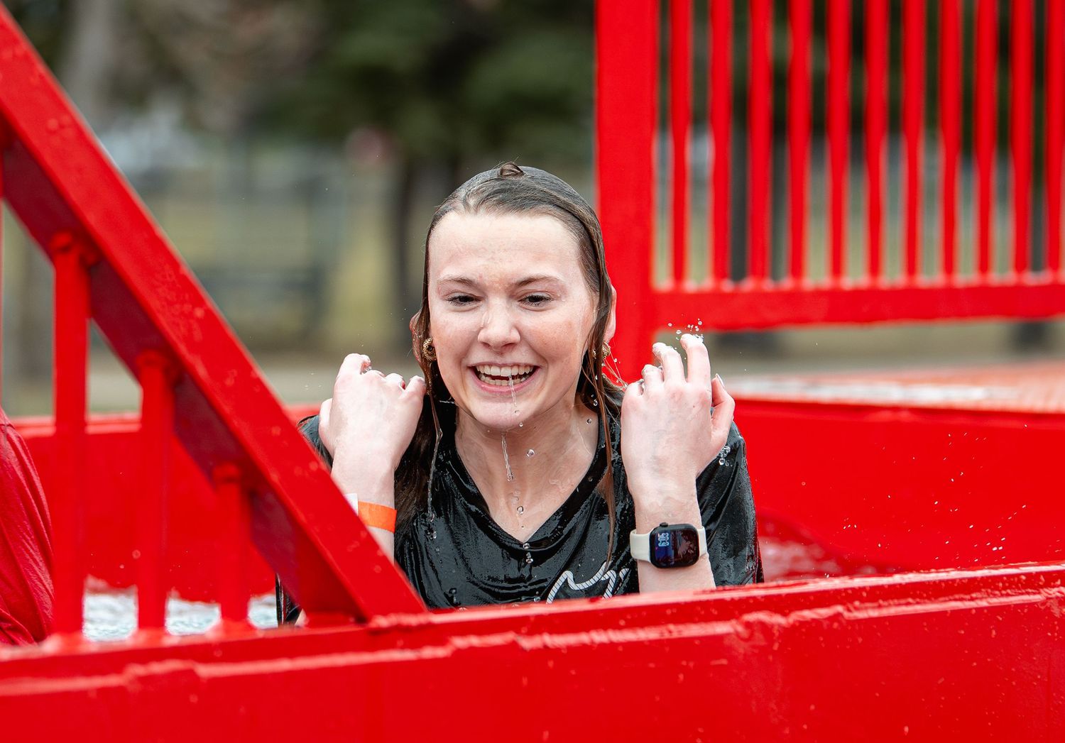 Excited woman emerging from a red dunk tank, soaking wet and laughing outdoors.