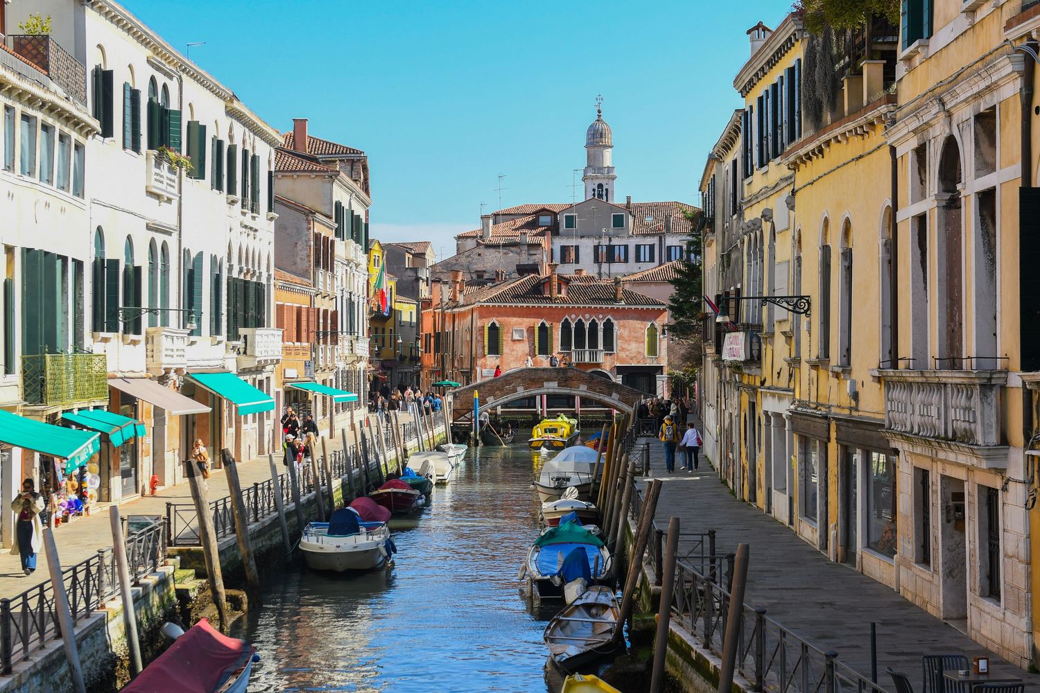 Picturesque Venice canal lined with pastel buildings and boats under bright blue sky.