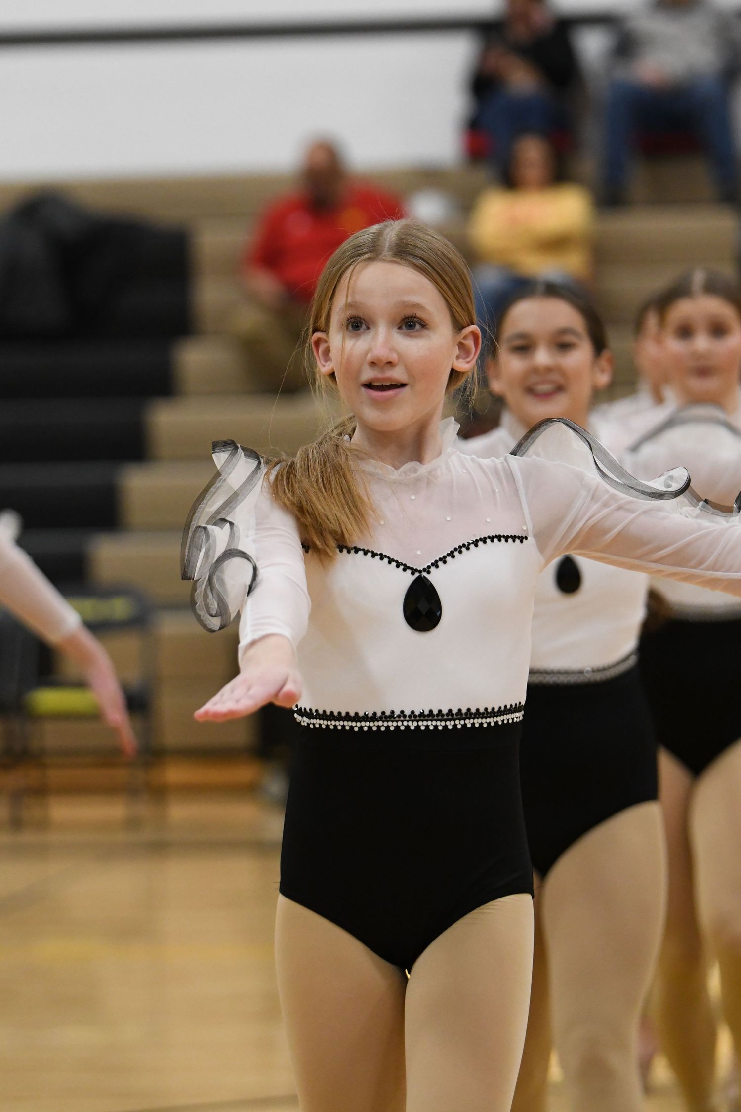 Performer in black and white costume with sheer sleeves dances during school performance.