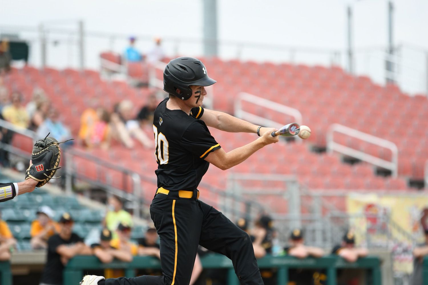 Baseball player in black and gold uniform takes a powerful swing at bat during game.