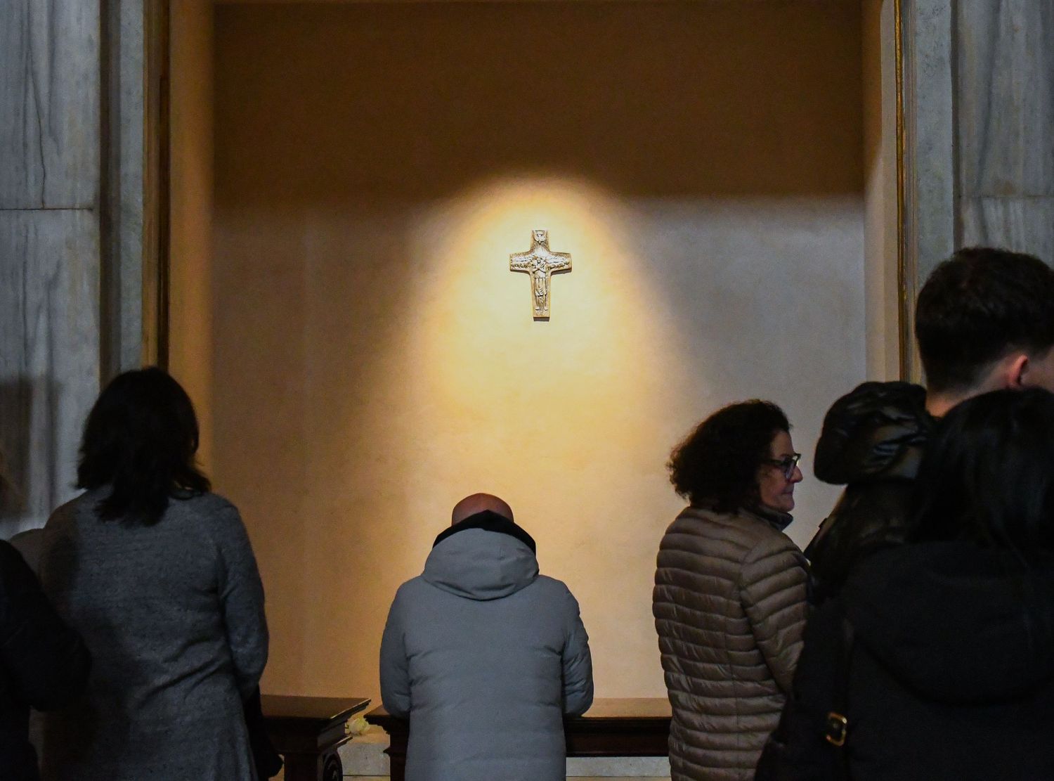 Dark church interior with people standing in silhouette against illuminated wall.